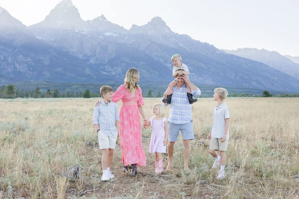 Parents walking with their kids through a field with mountain views near Jenny Lake Grand Teton during a family photo session