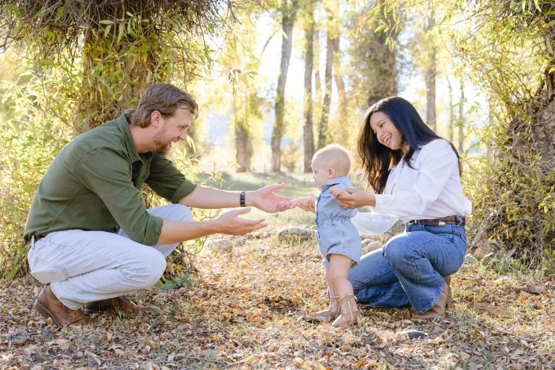 Parents encouraging their baby to walk during a playful and candid outdoor family photography session