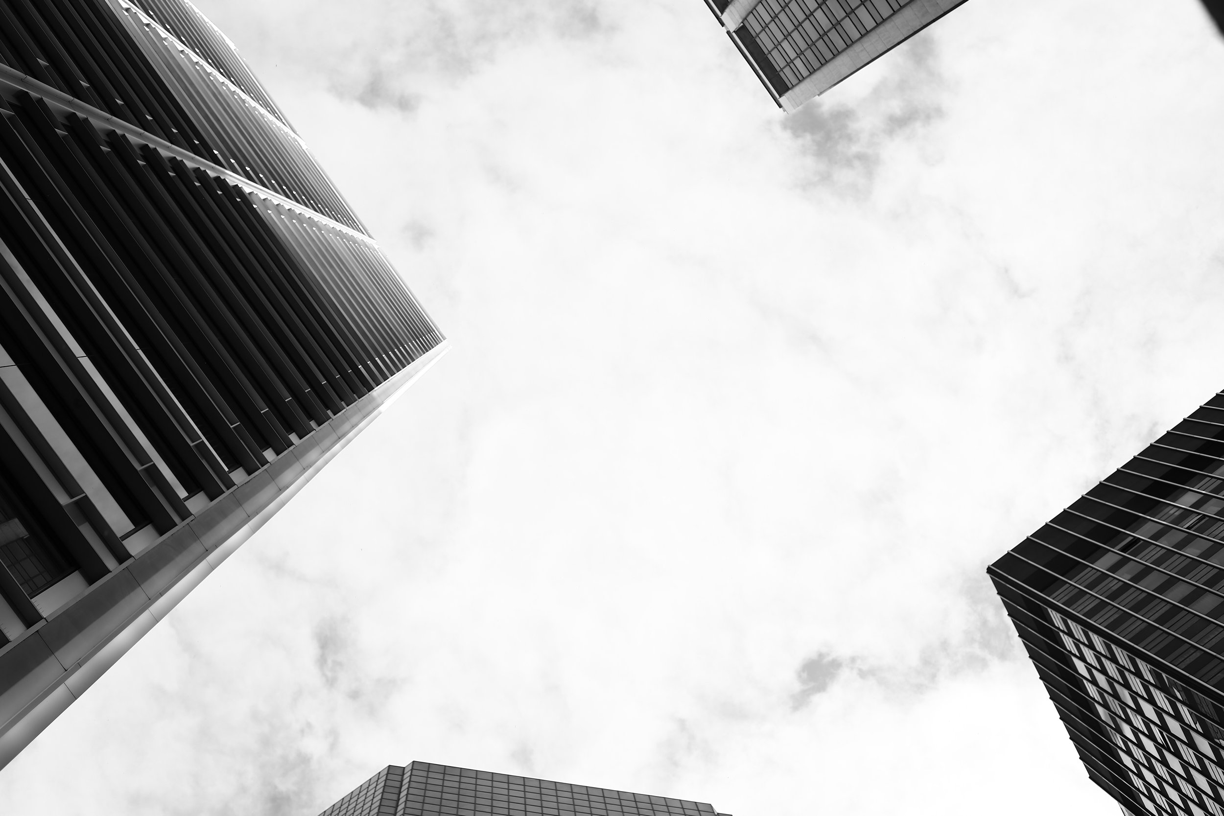 Black and white photo of three skyscrapers viewed from below against cloudy sky