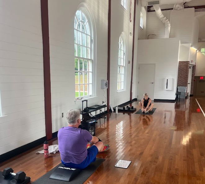 Man and woman facing each other doing Sit-ups in basketball gymnasium with large windows.