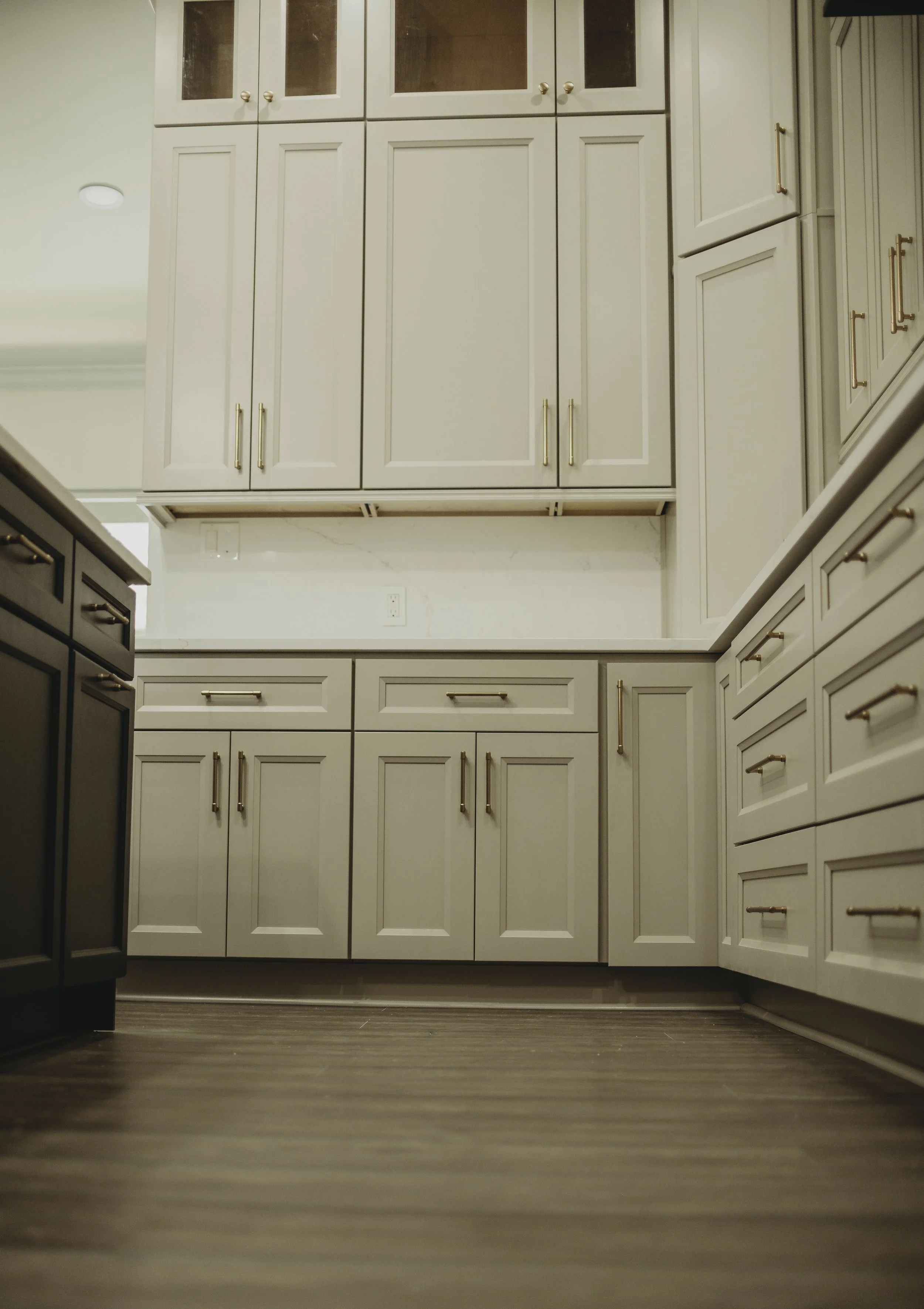 Low-angle photo of a modern kitchen with white cabinets and gold handles, dark flooring, and a partial view of a black appliance on the left.