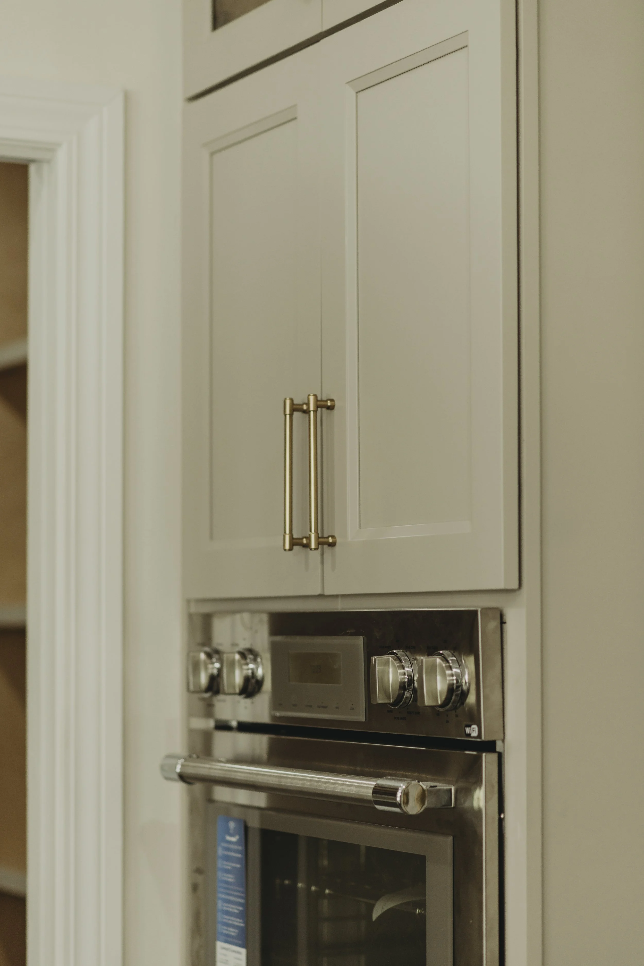 Close-up of a kitchen wall oven with metallic knobs and a handle, built into cabinetry with beige doors and gold handles.