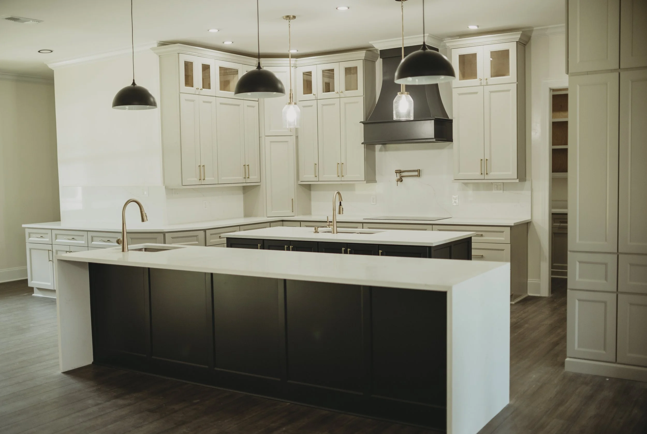 Modern kitchen with white cabinets, dark island, and three black pendant lights hanging from ceiling.