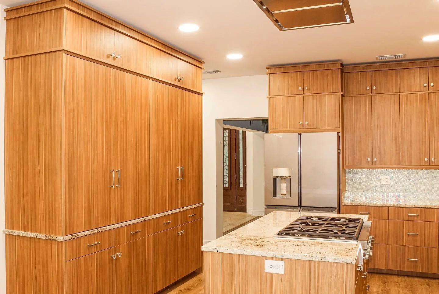 Kitchen with wooden cabinets, granite countertops, a stainless steel refrigerator with a water dispenser, a stove on the island, and recessed ceiling lights.