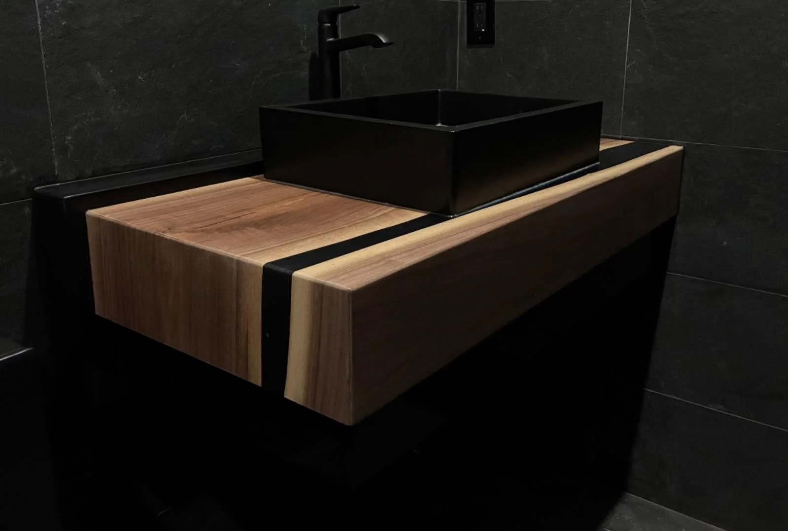 Luxury High End Epoxy Live Edge Modern bathroom sink with a black rectangular basin on epoxy live edge countertop, set against dark tiled walls.