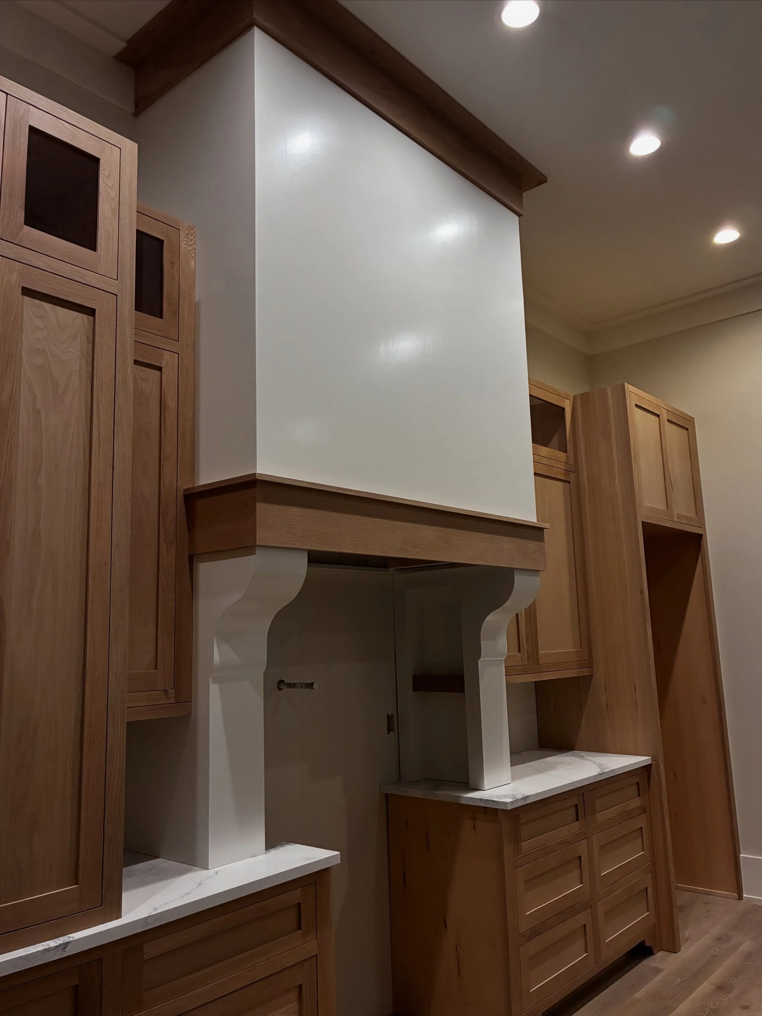 Kitchen cabinets with a white wall and marble countertop, with recessed lighting in the ceiling.