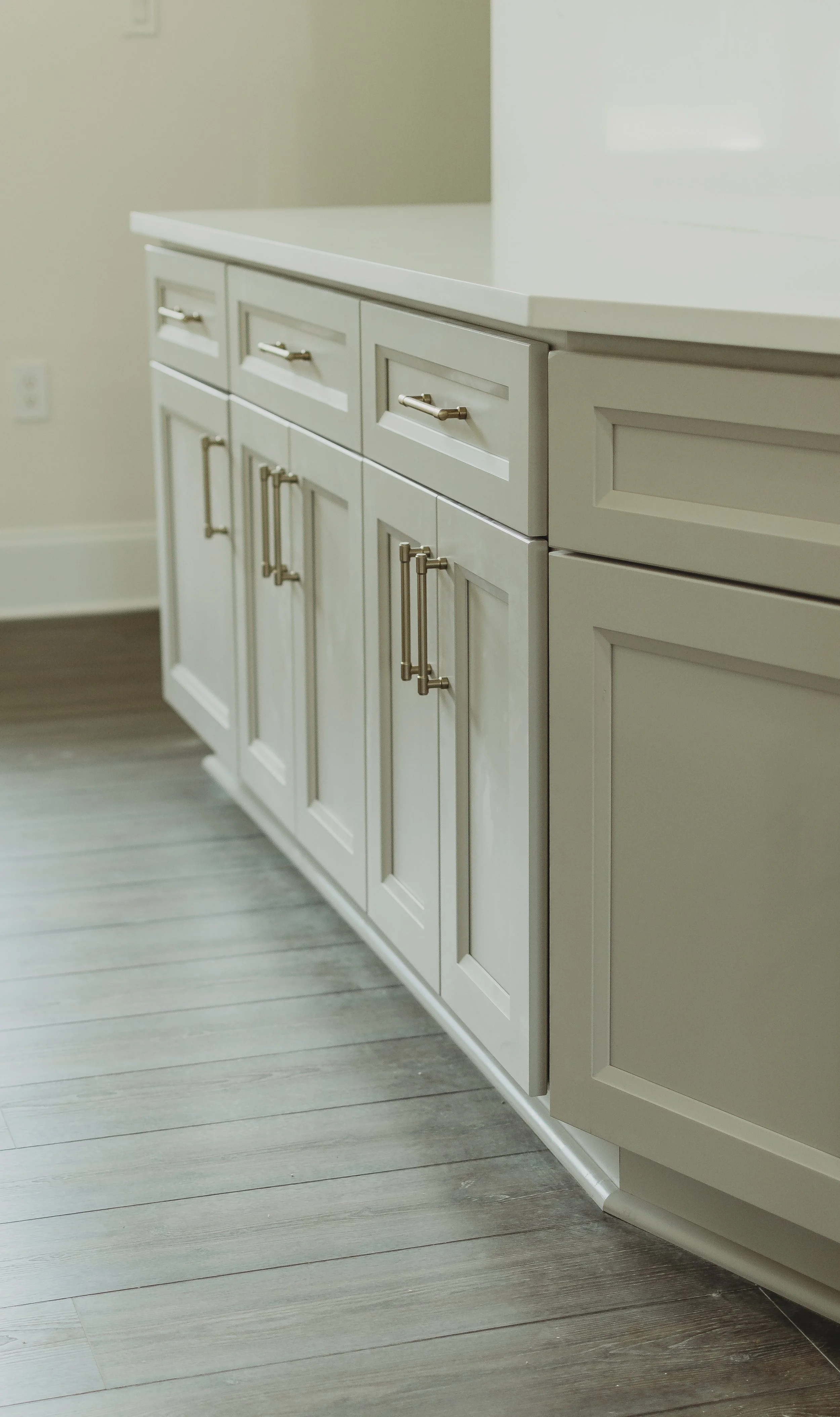 Close-up of a white kitchen cabinet with silver handles, on a light gray wooden floor.