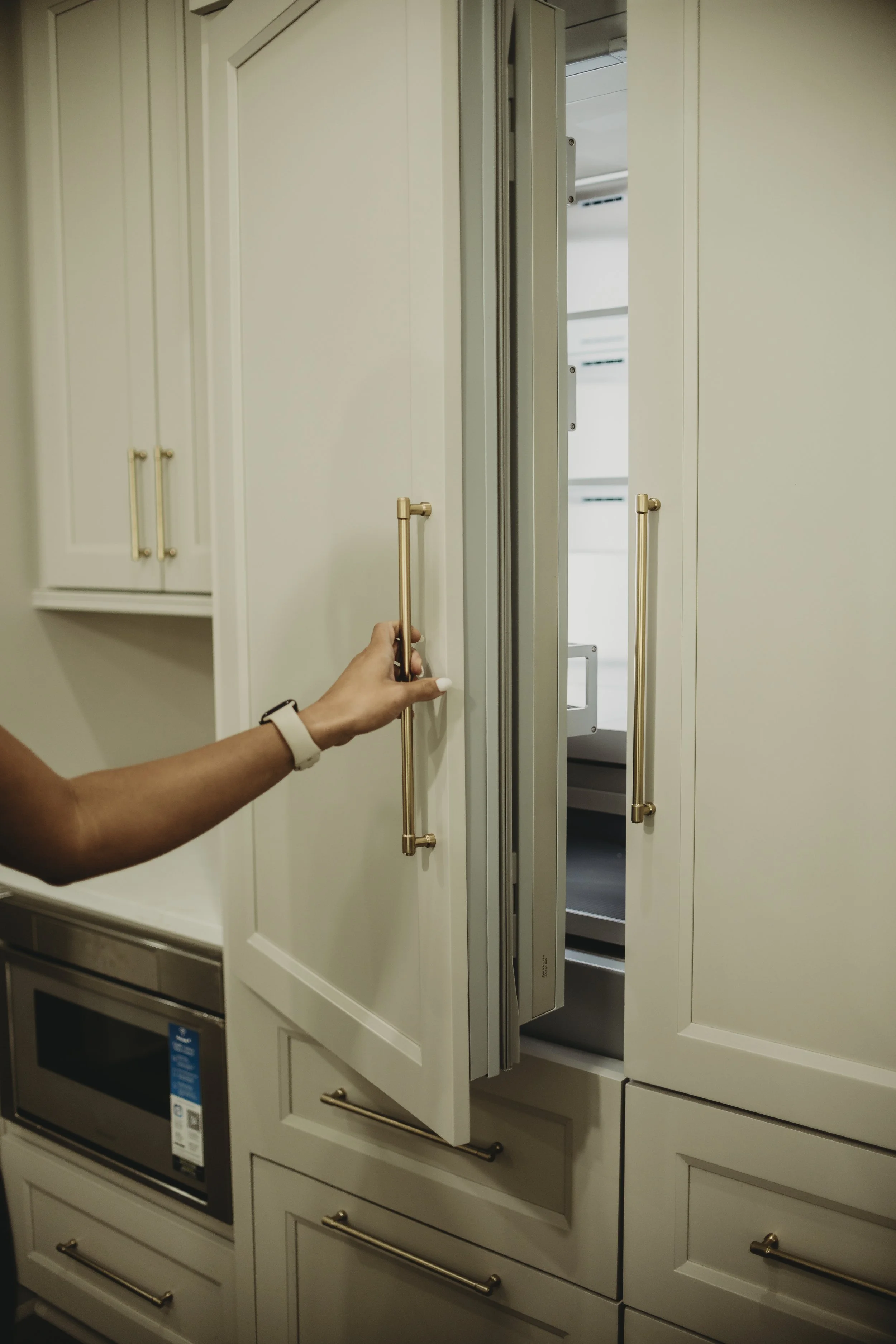Person opening a custom cabinet refrigerator door in a kitchen. The cabinet has gold handles and there are other cabinets and an oven visible.
