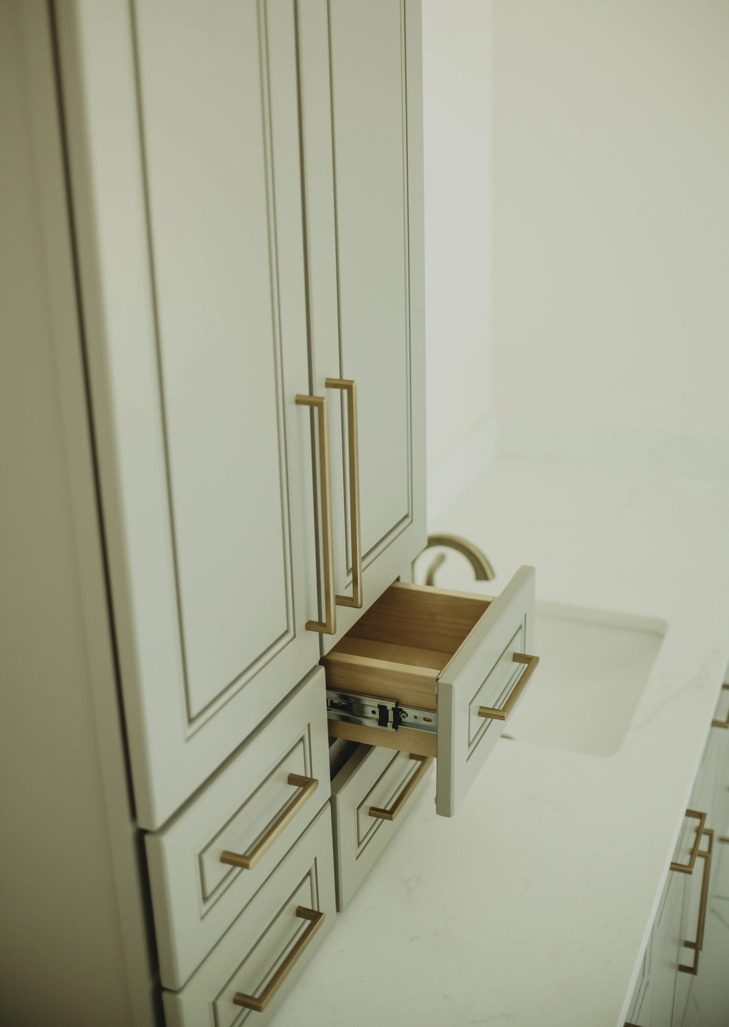 A cream-colored kitchen cabinet with gold handles, with one drawer pulled out showing the drawer mechanism inside.