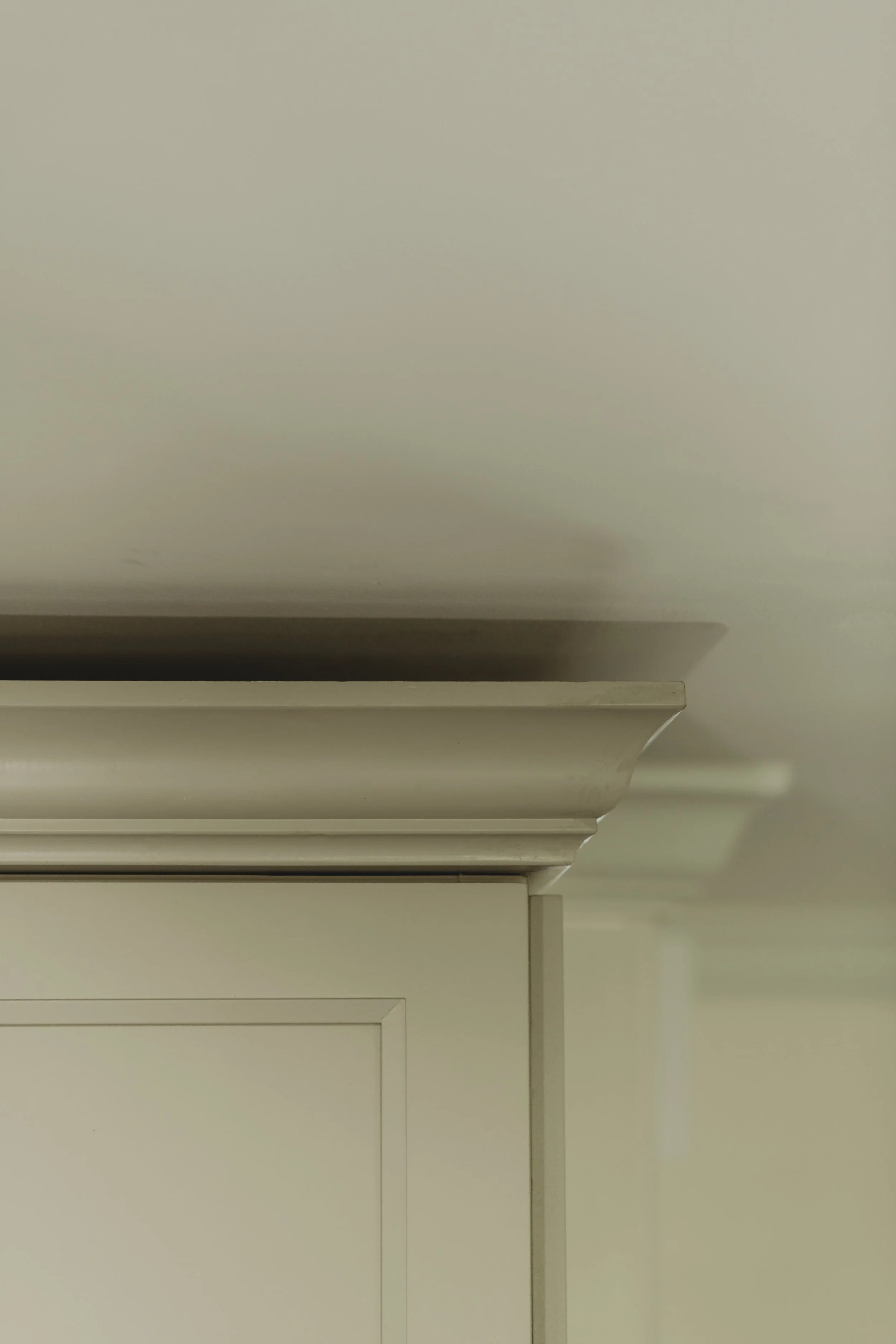 Close-up of the corner of a beige or off-white piece of furniture, possibly a cabinet or dresser, with crown molding detail at the top.