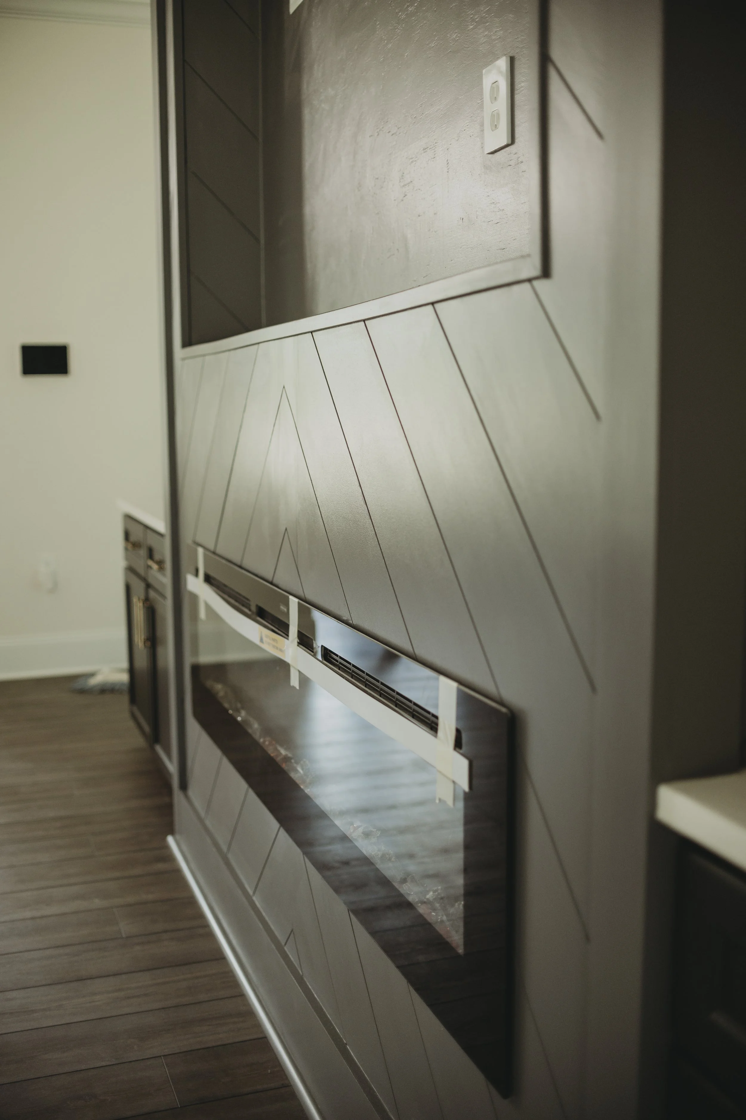 Close-up of a modern built-in wall oven with a black glass door, situated in a kitchen with wooden flooring and gray cabinetry.