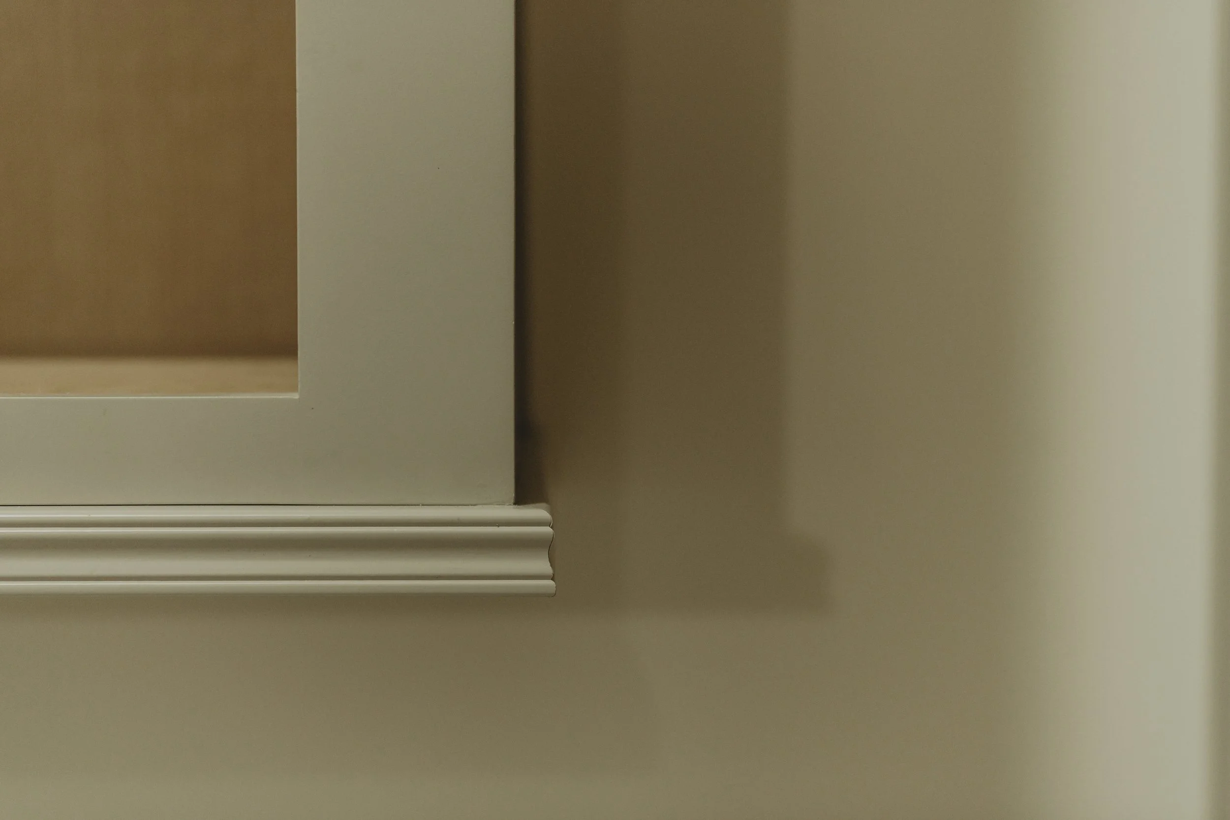Close-up of pebble cabinet with decorative light rail molding detail at the bottom, mounted on a beige wall.
