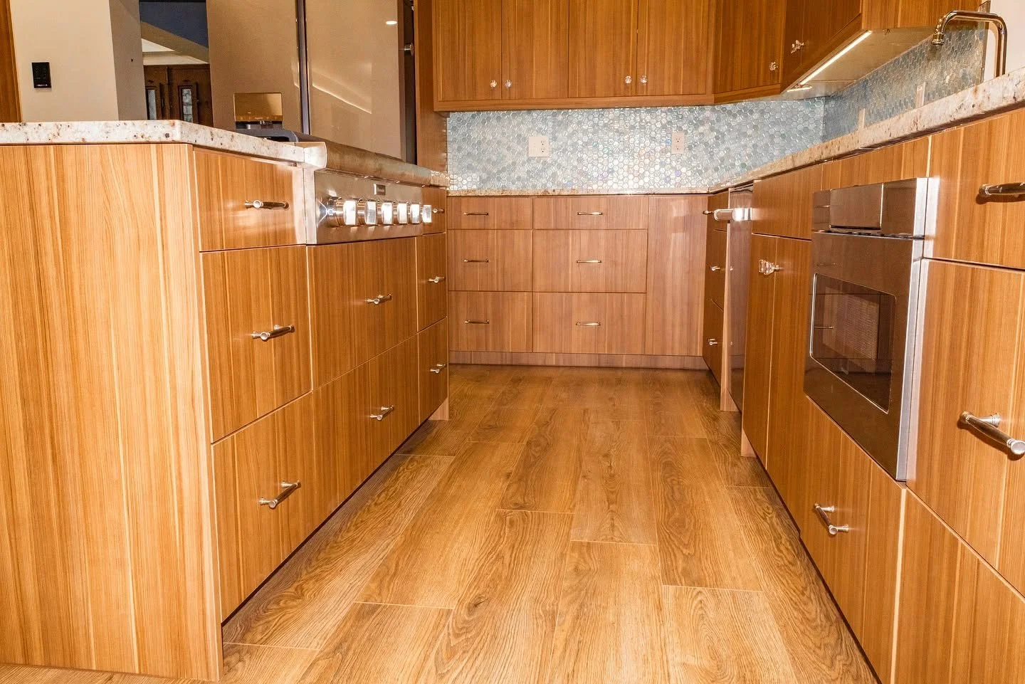 Wooden kitchen cabinets with stainless steel appliances, marble countertop, and a tiled blue backsplash.