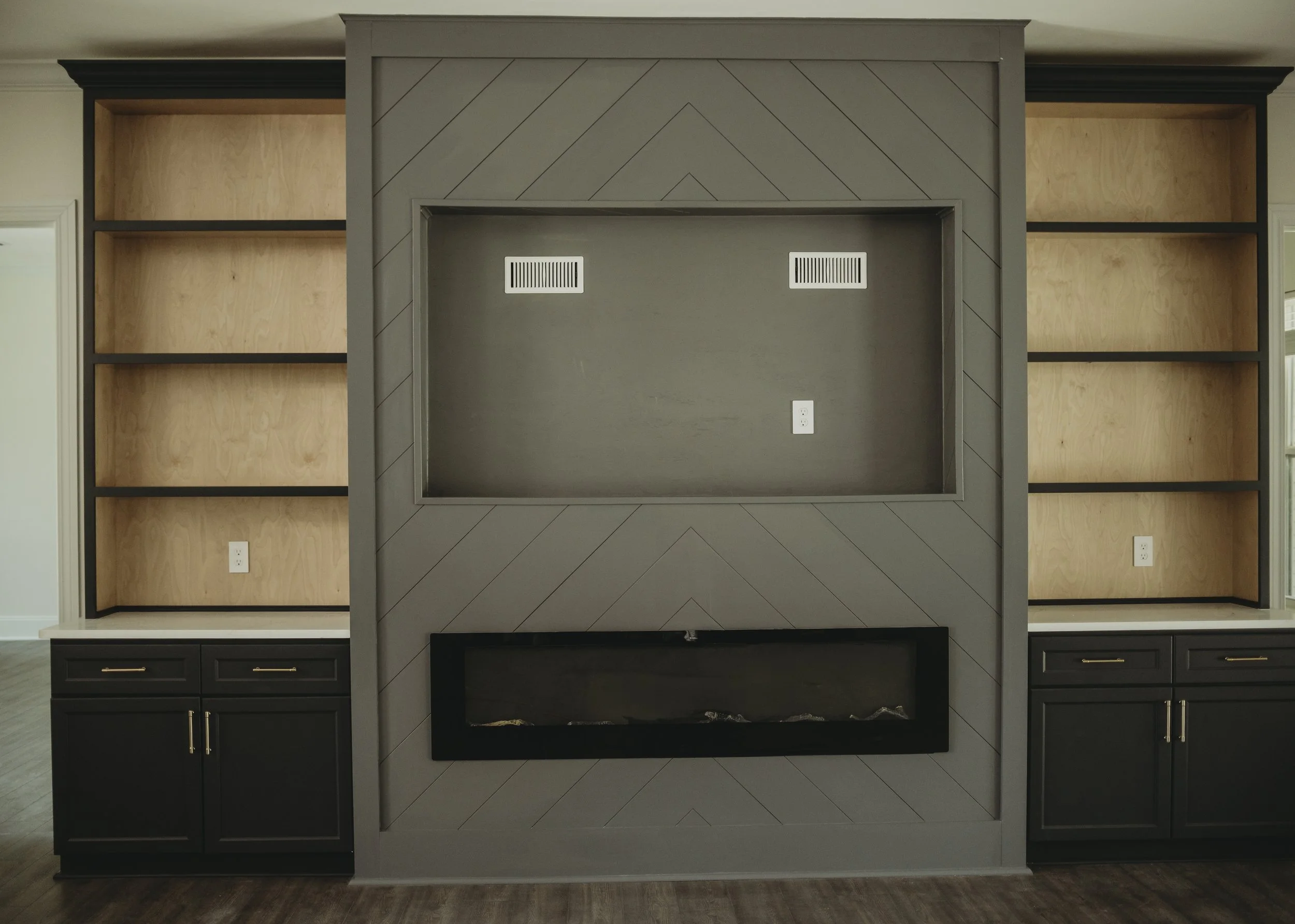 Empty fireplace with gray framing and black cabinet base, flanked by built-in wooden bookshelves, in a living room.
