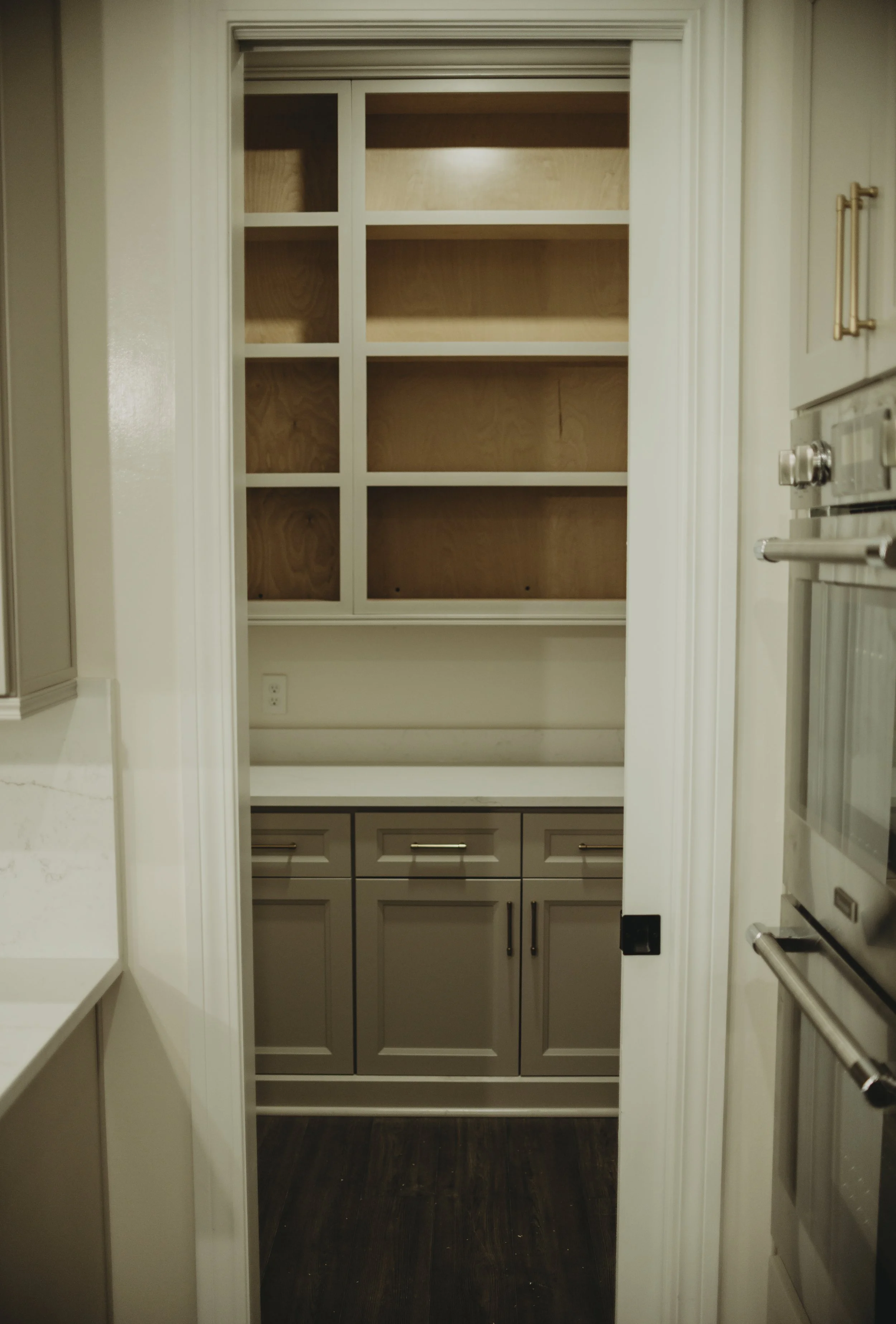 Empty kitchen pantry with wooden shelves and beige cabinets below, situated in a small room with white walls and dark wood flooring.