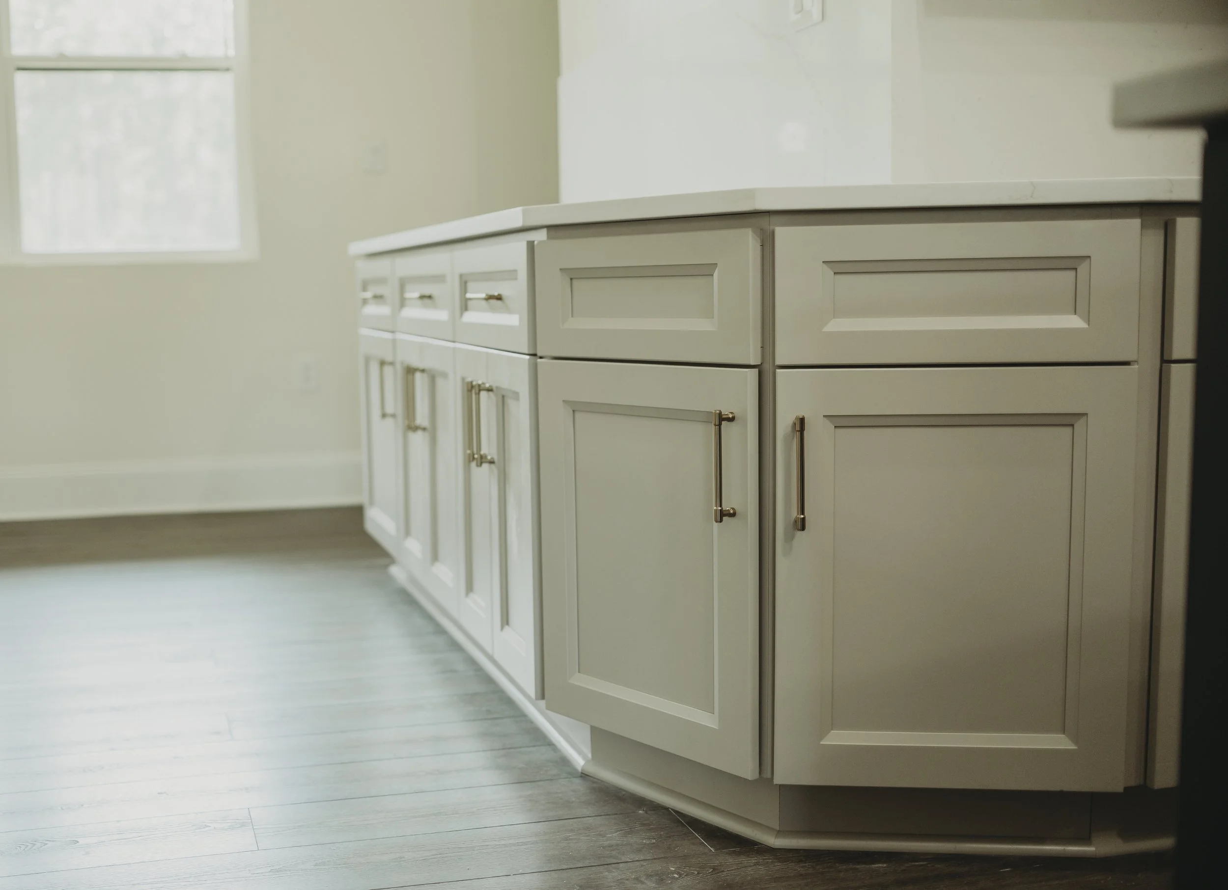 Custom Breakfast nook, a beige kitchen cabinet with gold hardware, set against a light-colored wall with a large window in the background, and a light-colored wood floor.