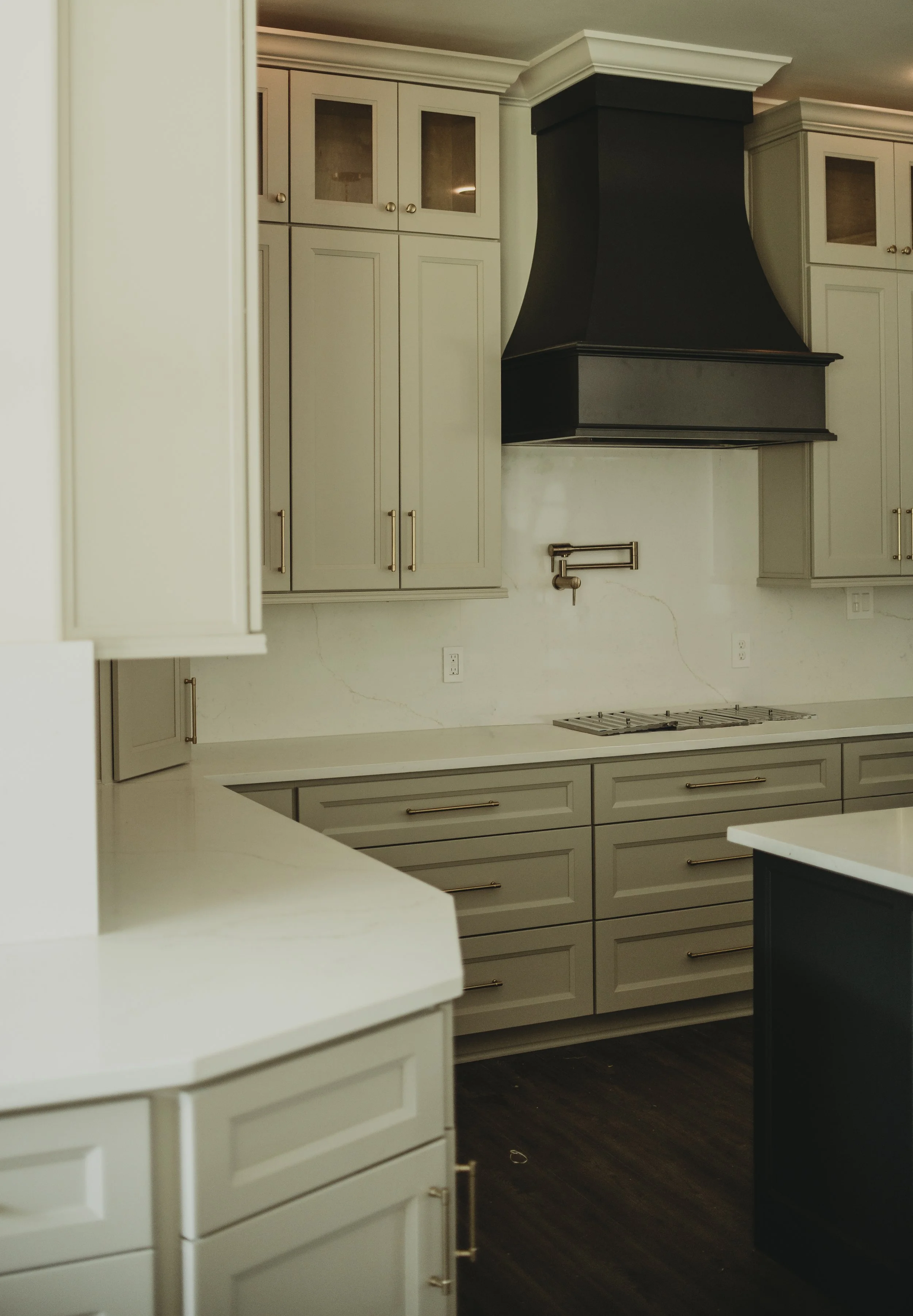 A kitchen with white cabinets, a black range hood, and dark hardwood floors.