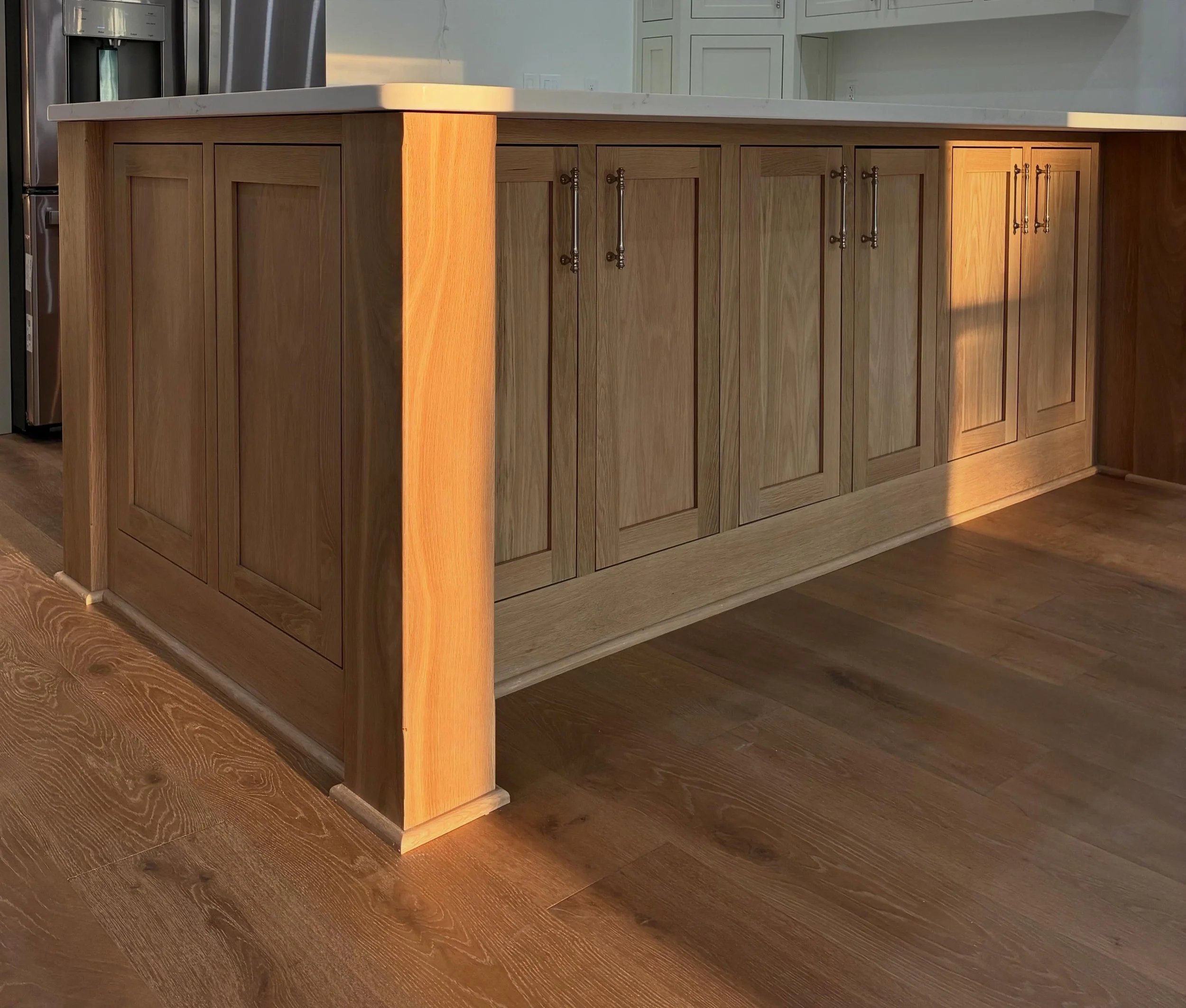 Luxury White Oak Wooden kitchen cabinets with brass handles beneath a white marble countertop, next to stainless steel refrigerator in a modern kitchen.