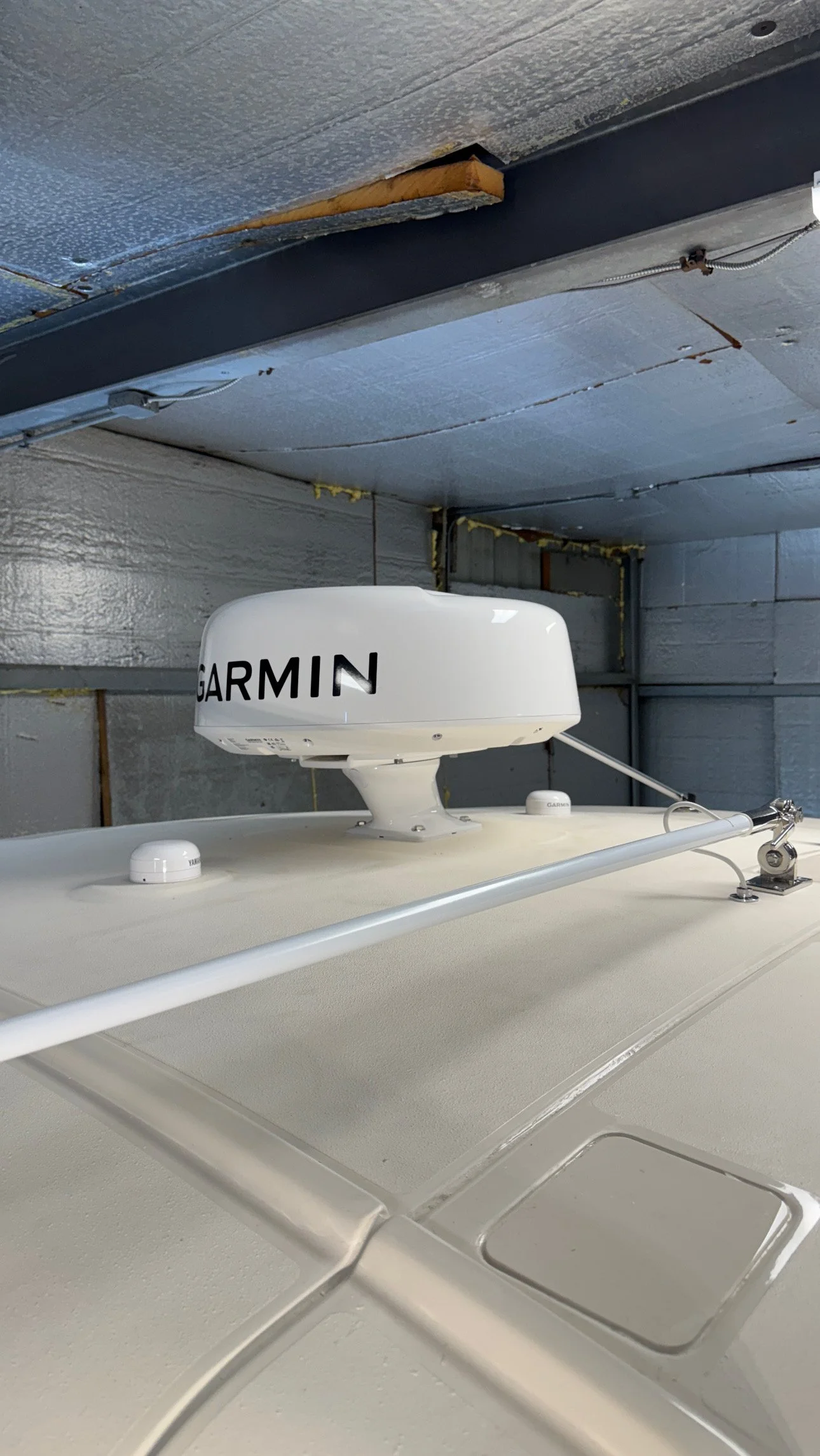 Close-up of a Garmin radar antenna mounted on the roof of a vehicle, with a metal awning and insulation in the background.