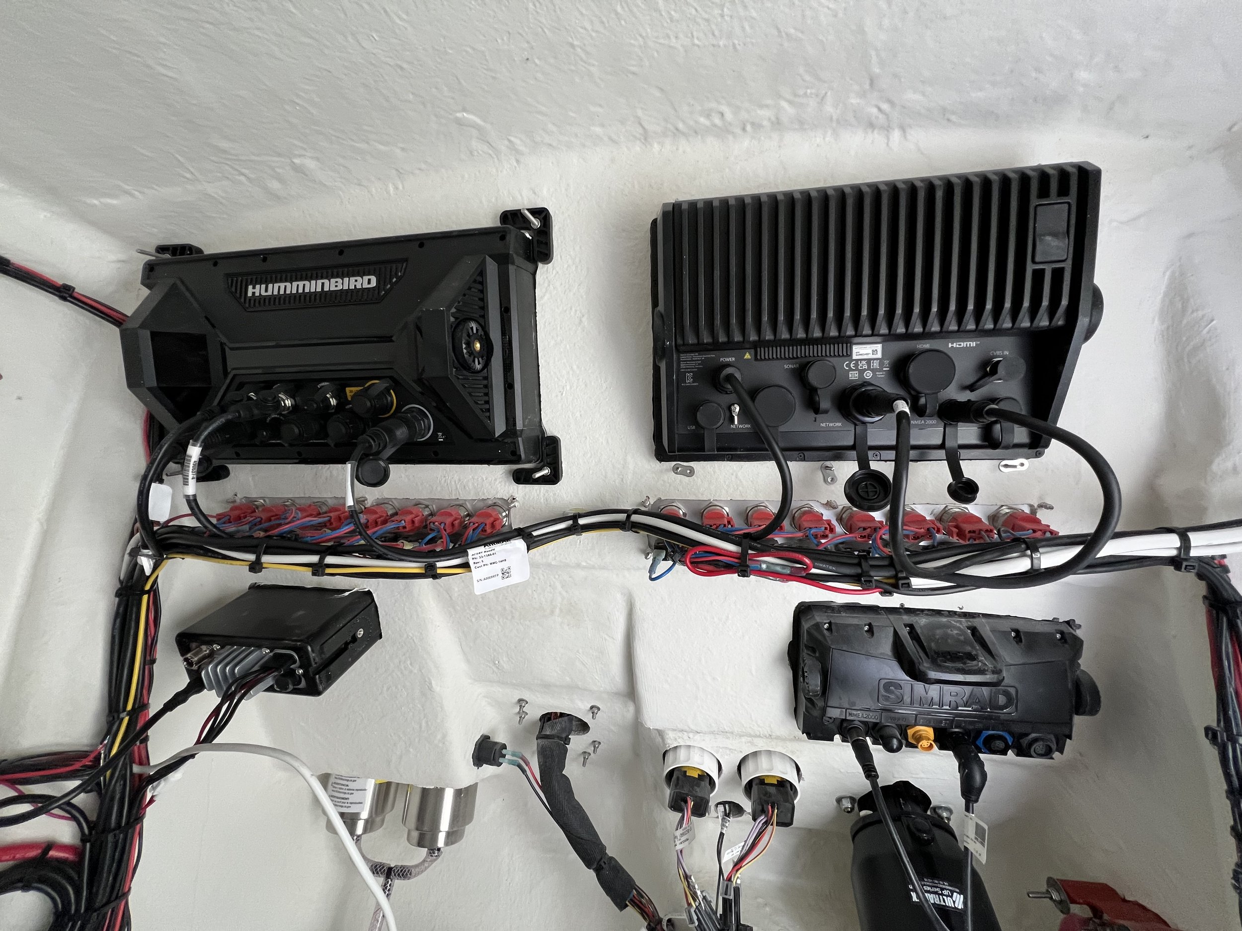 Electrical wiring and electronic components mounted on a white wall, including a Humminbird device, control panels, and connectors.