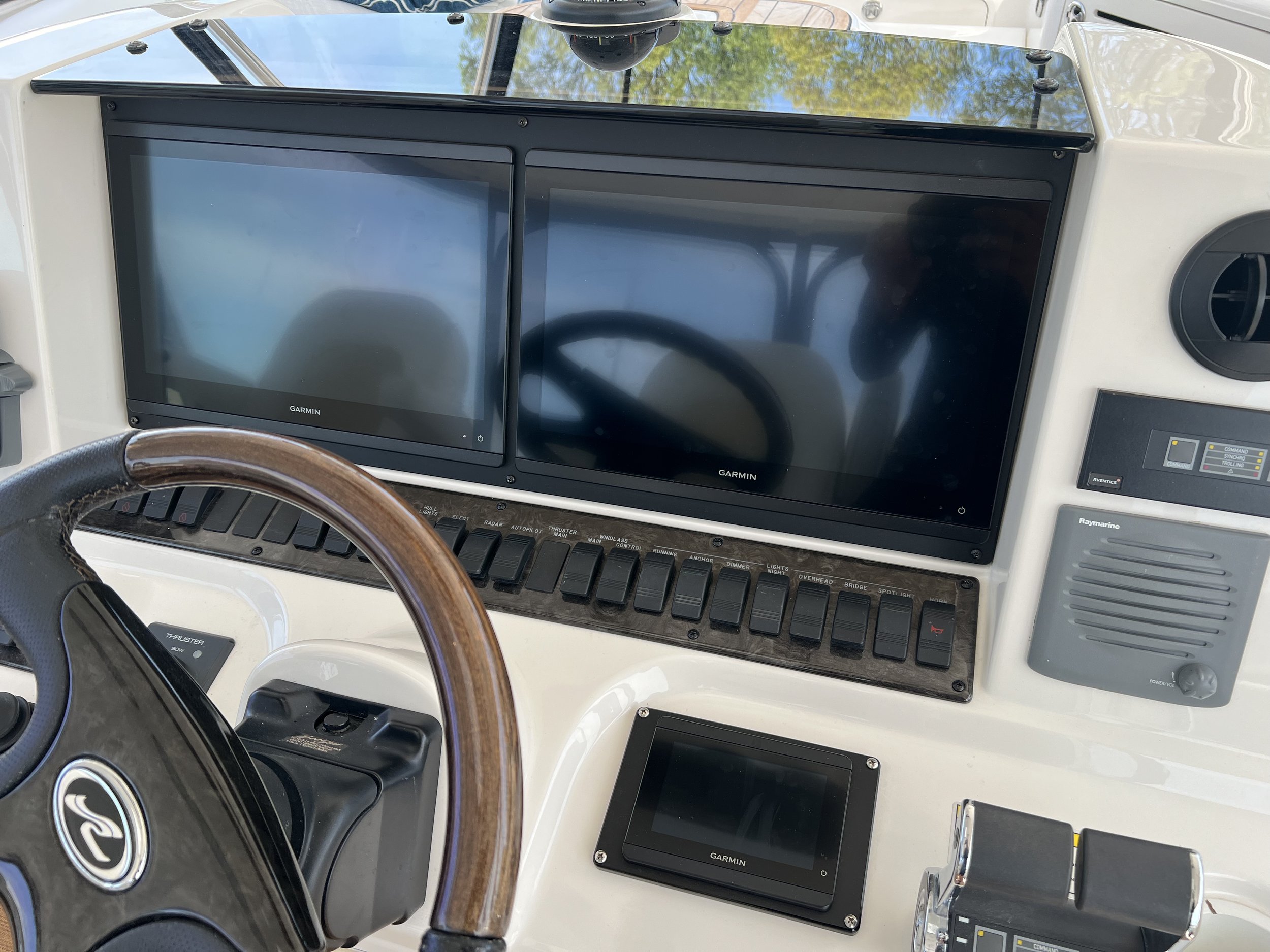 Close-up view of a boat helm with garnin GPS and radar screens, switches, and control devices.