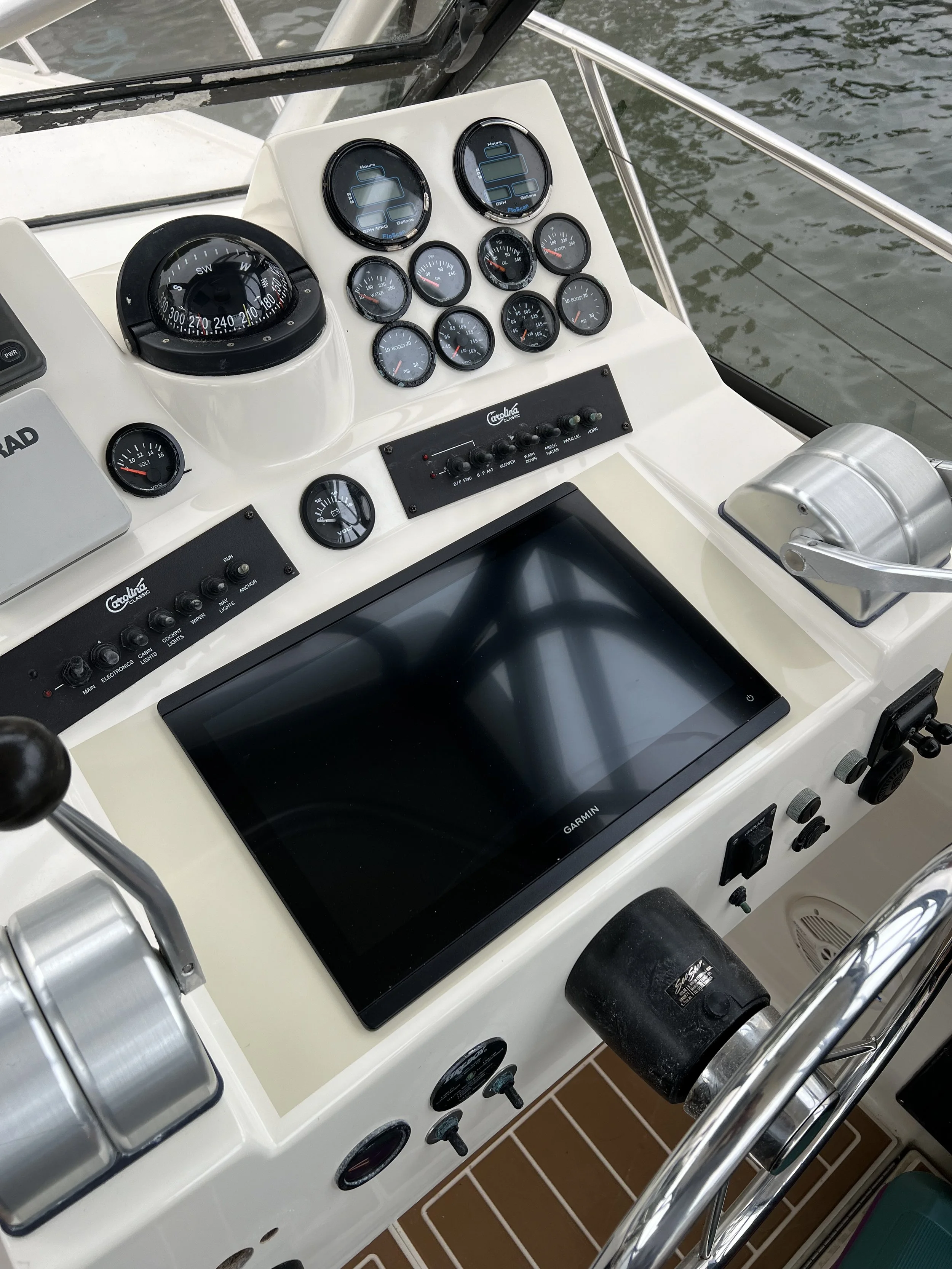 Boat helm with various gauges, a Garmin screen, and a steering wheel.