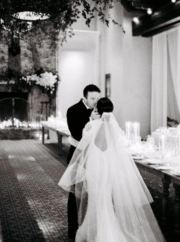 A bride and groom sharing a moment during their wedding reception in an indoor venue with elegant decor and table settings.