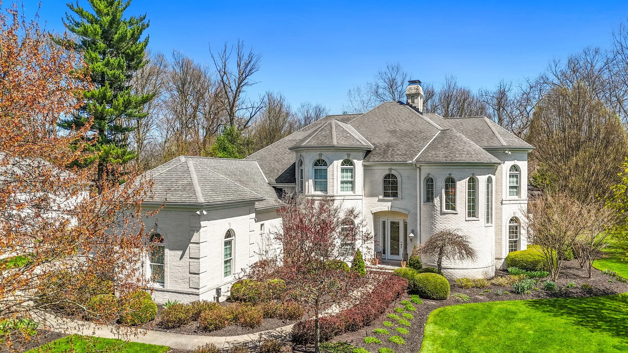 A large, white brick house with multiple gabled roofs surrounded by trees and landscaped gardens.