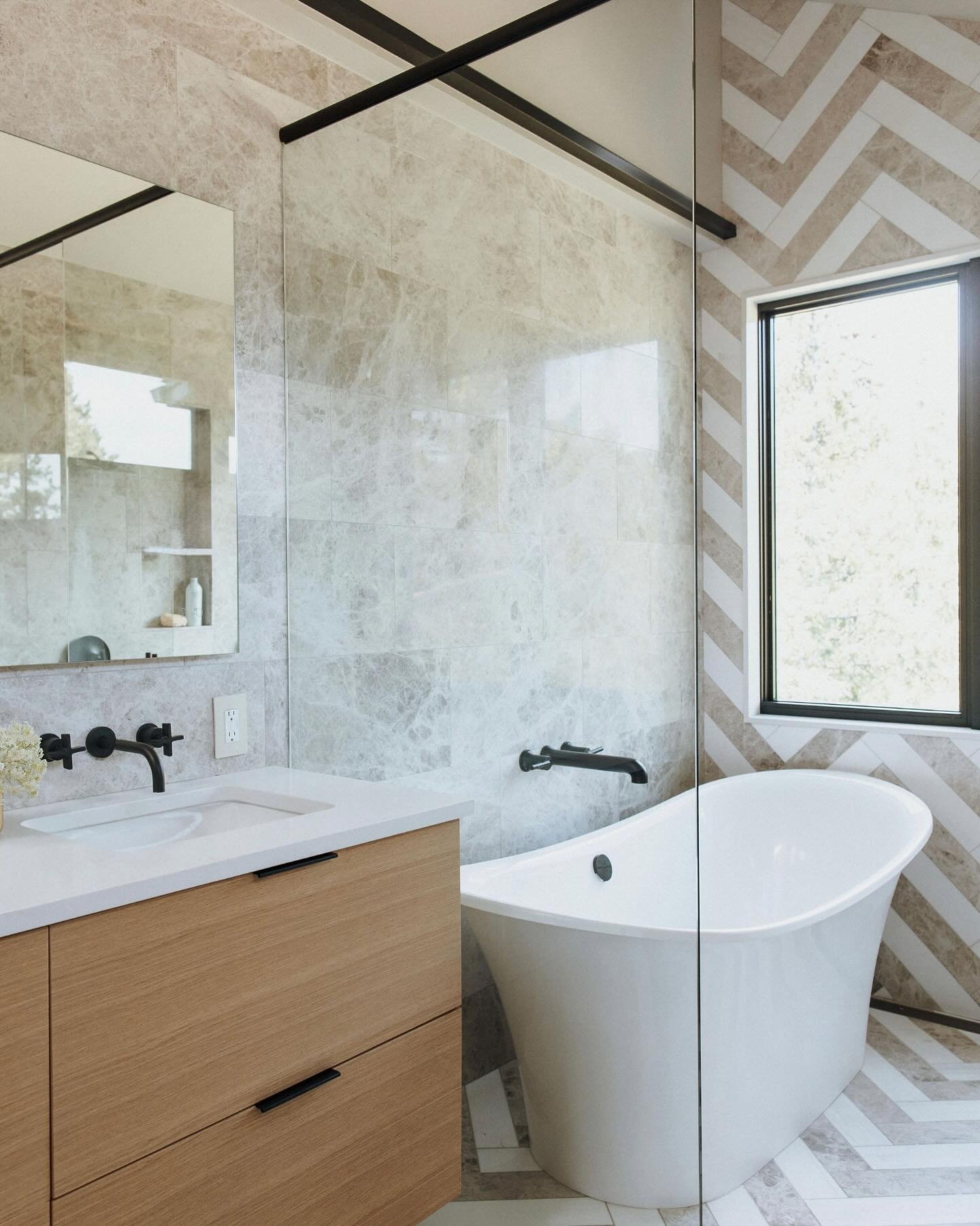 This primary bath was all about balance&mdash;warm wood, cool stone, clean lines. The chevron tile adds just enough pattern without overwhelming the space. We kept the details simple: minimalist edge pulls on the vanity, dual shower heads flanking a 