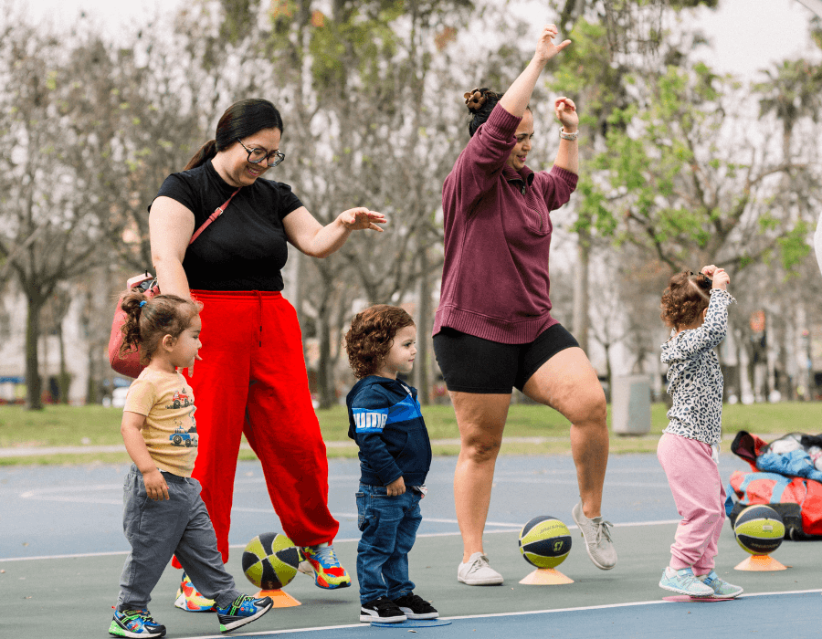 Two women with four children playing basketball on an outdoor court.