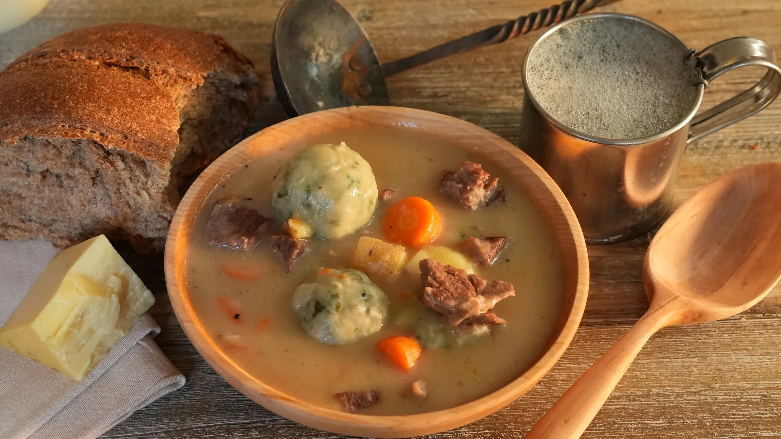 wooden bowl of meat and vegetable stew with round dumplings