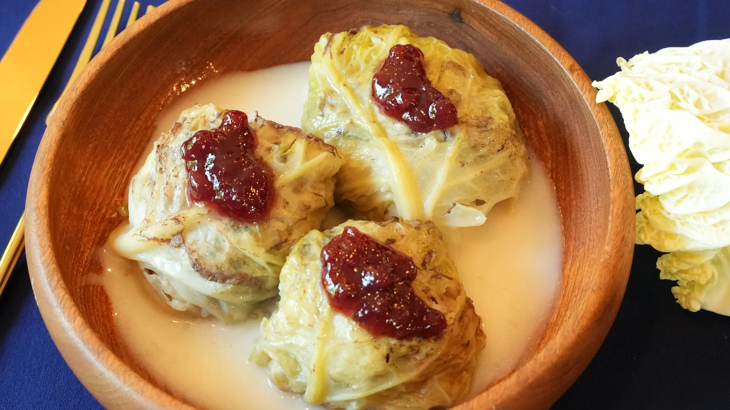 3 spherical cabbage rolls in a creamy sauce with lingonberry jam