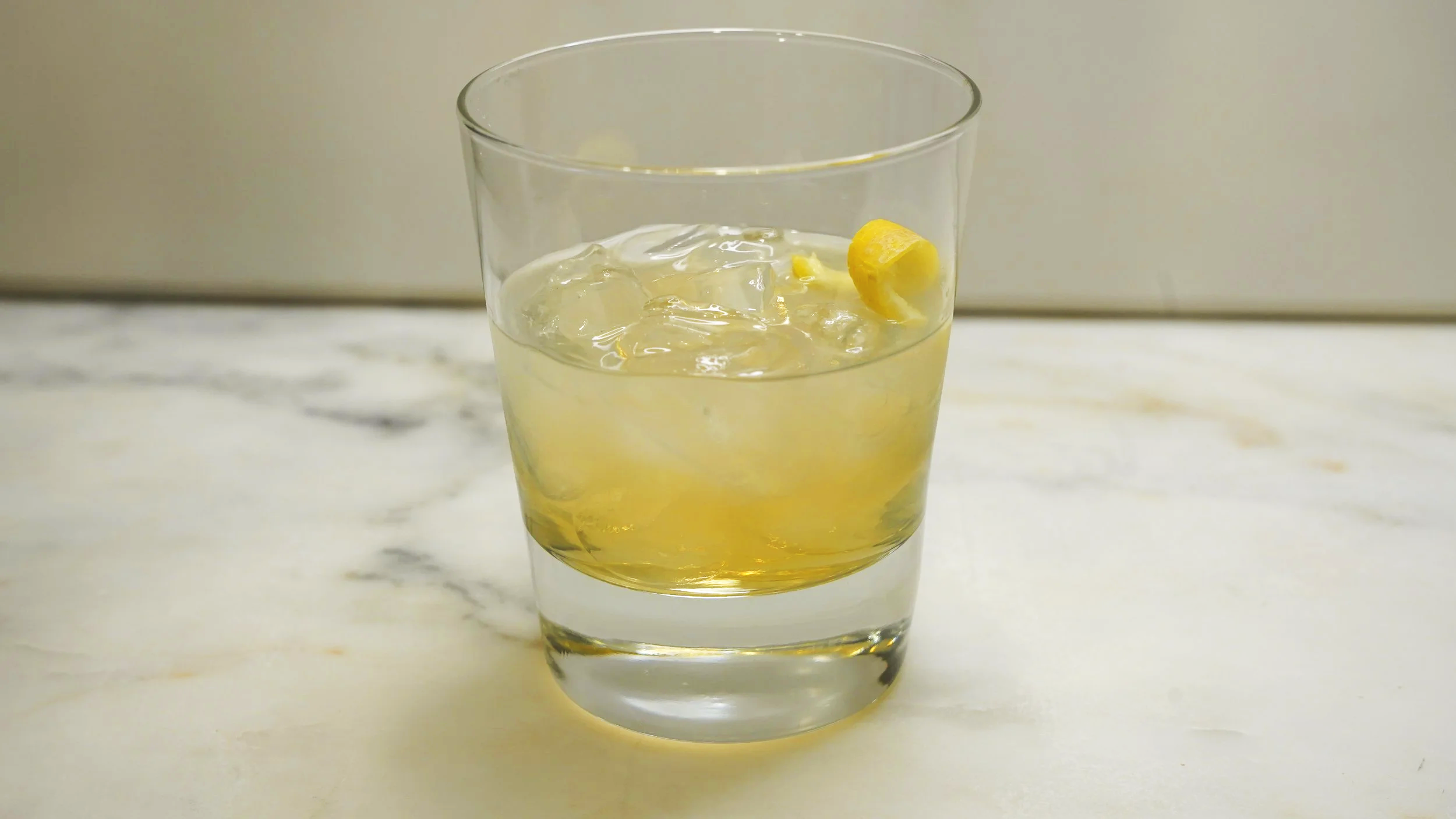 slightly cloudy yellow cocktail with ice and lemon twist