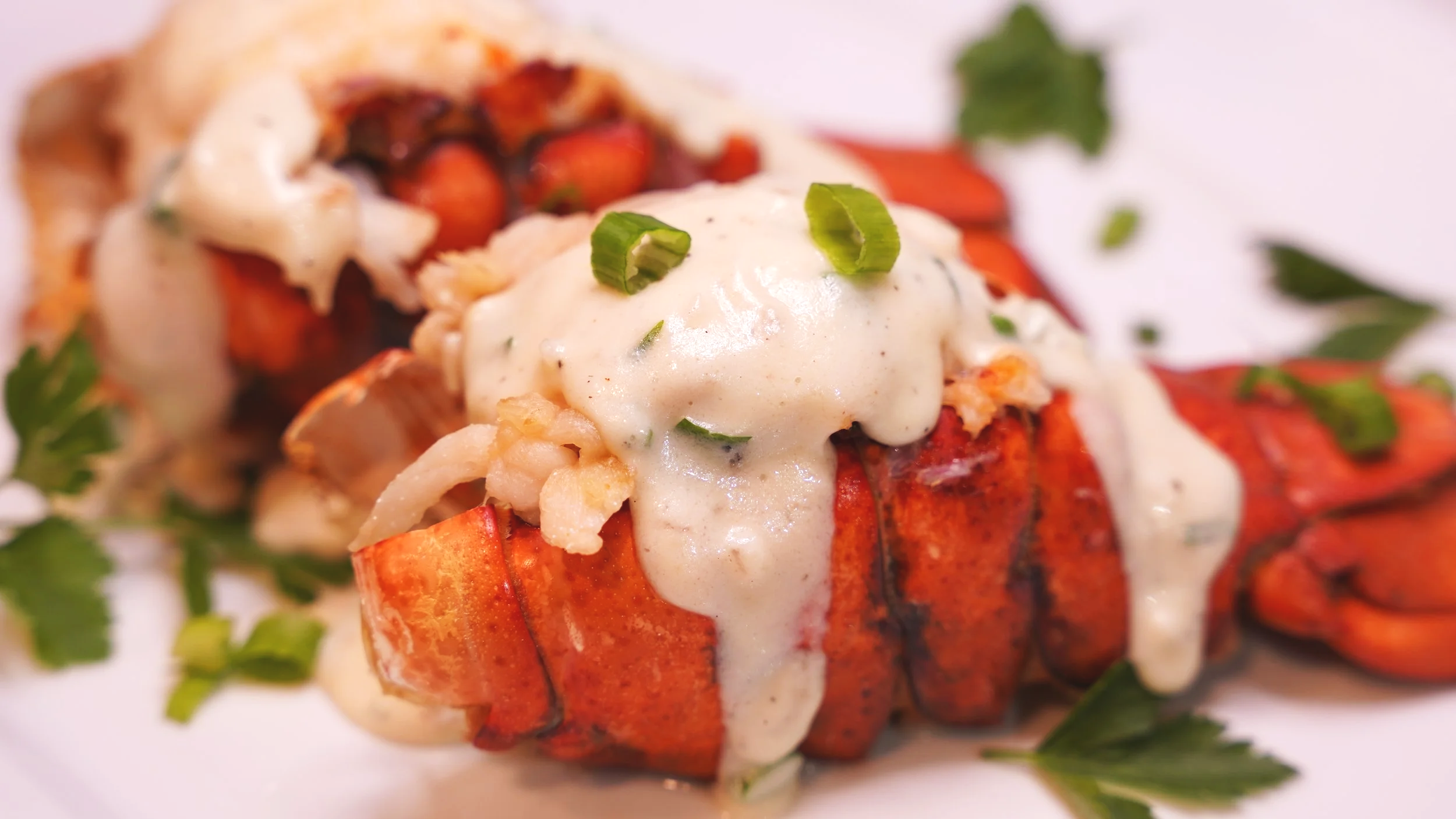 lobster tails with creamy white sauce garnished with scallions and parsley