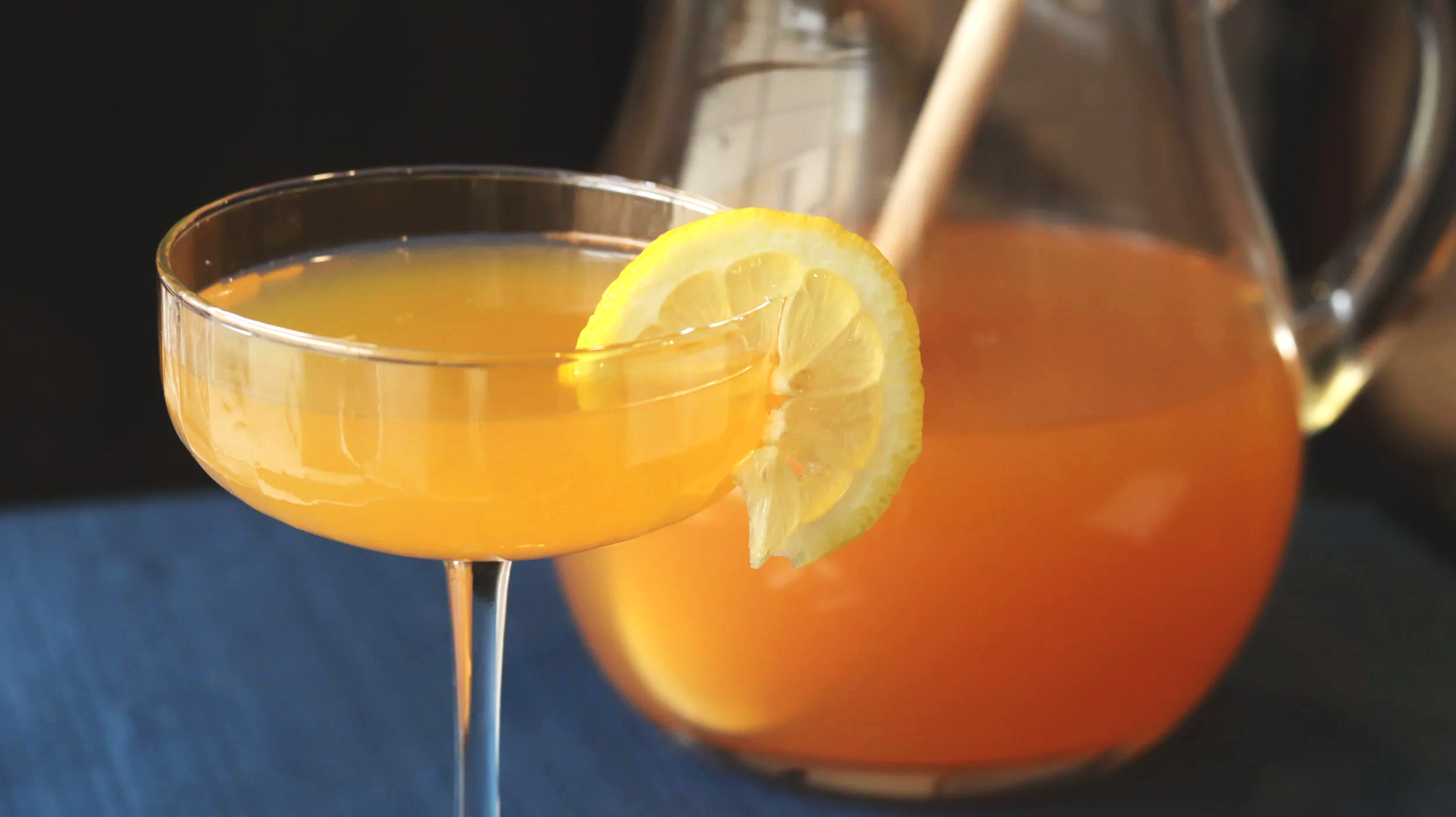 slightly cloudy orange-colored cocktail garnished with a lemon slice