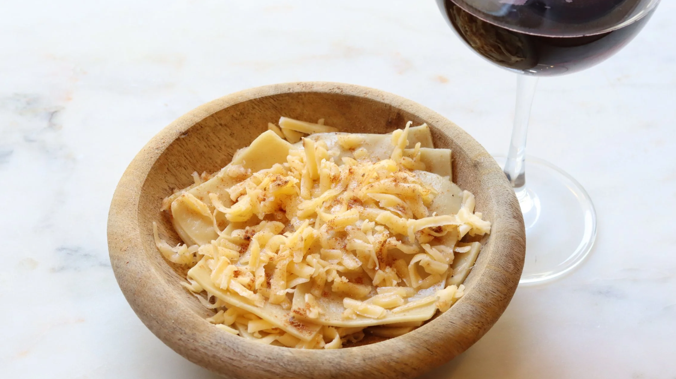 wooden bowl with squares of homemade pasta layered with grated gouda and spices
