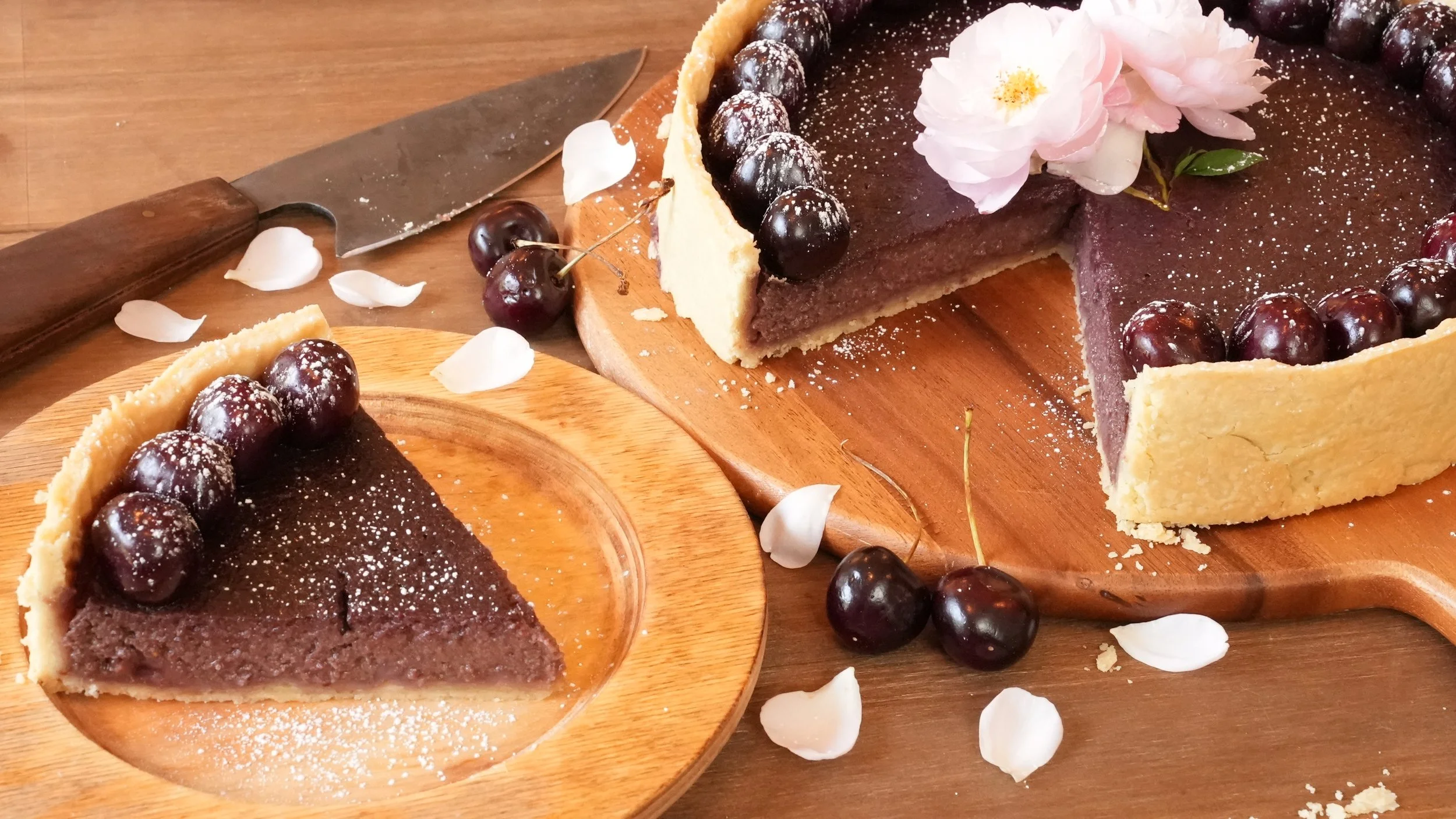 dark cherry cheesecake in pastry crust decorated with whole fresh cherries, powdered sugar, and fresh roses