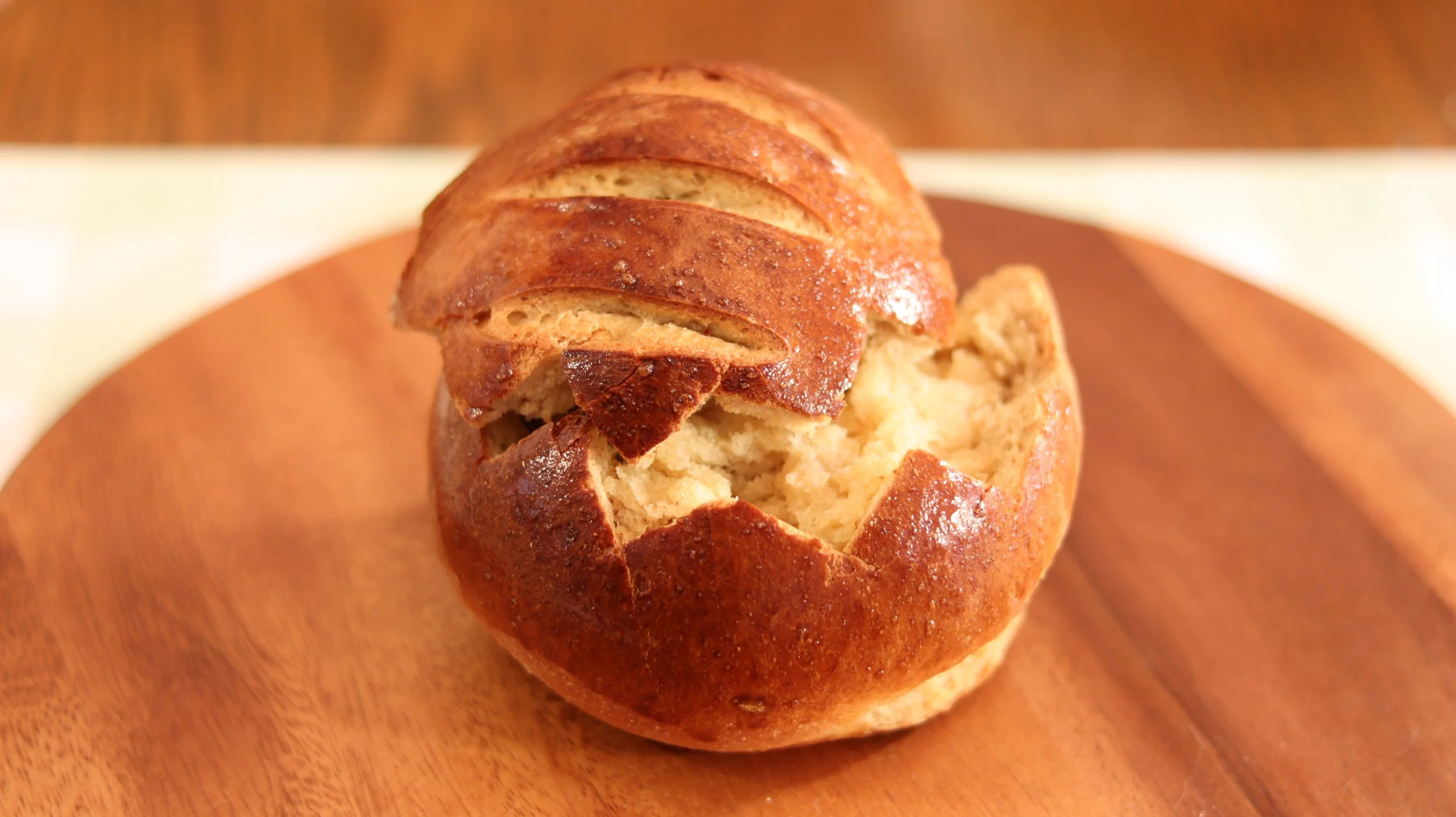 bread roll with top cut off in zigzag pattern shiny dark crust with three score marks on top