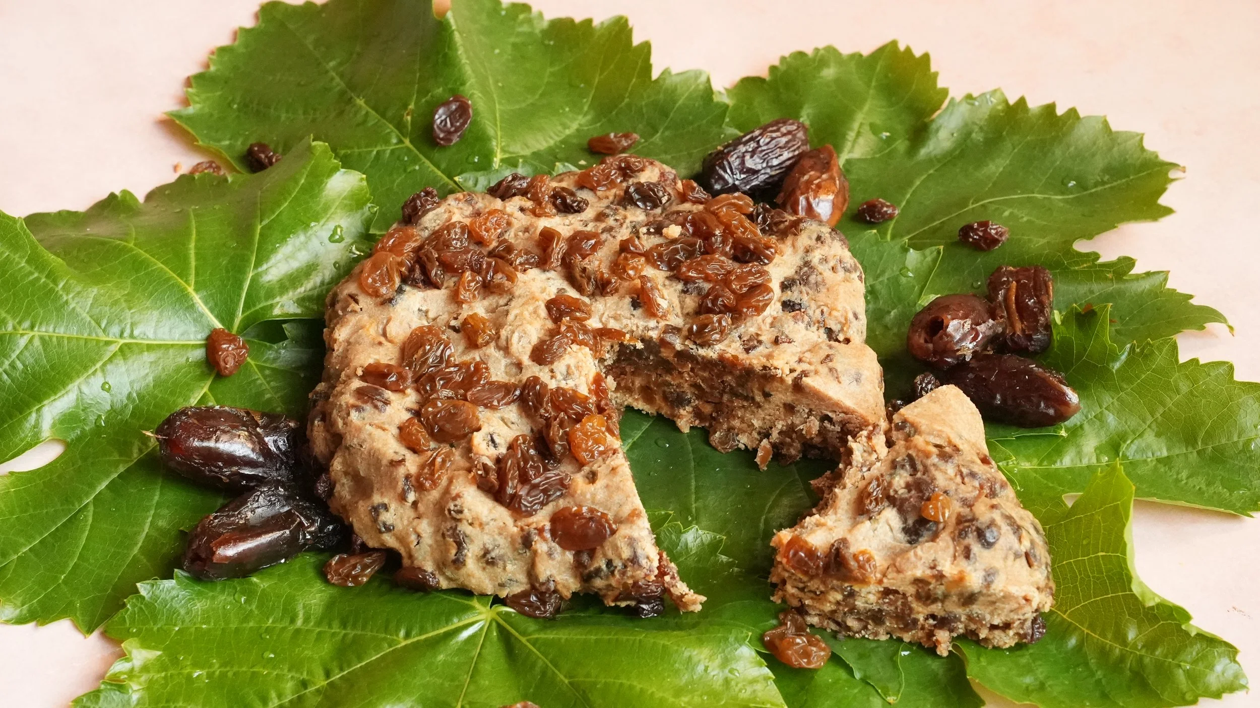 disc of dense cake studded with ground dates and topped with raisins on a bed of fresh grape leaves
