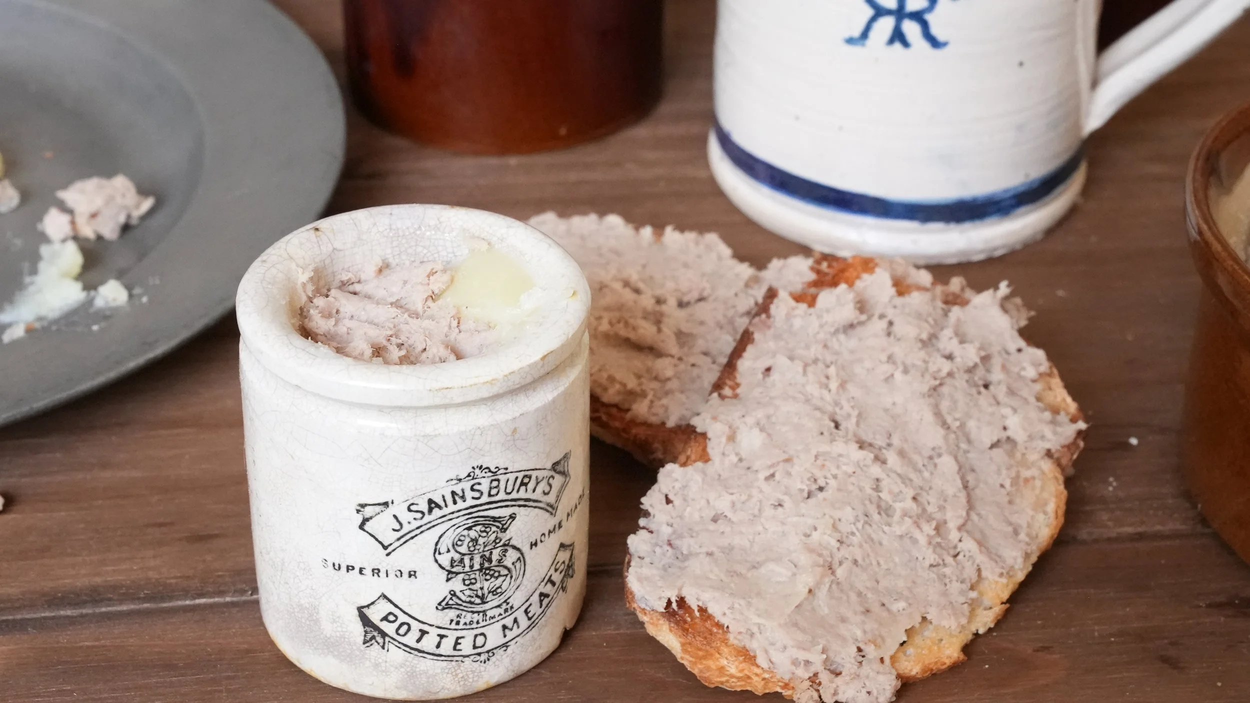 ceramic jar filled with paste made from pounded roast beef, spices, and butter. Slice of toast with potted beef spread over it