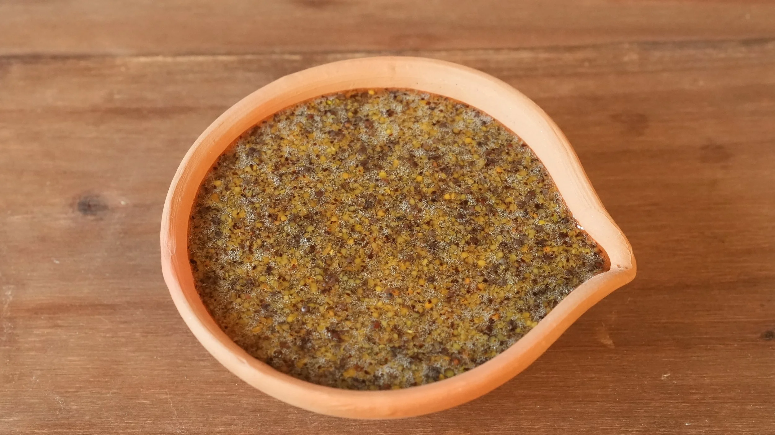 coarse ground mustard with honey, vinegar, and olive oil in a small clay bowl with a pouring lip