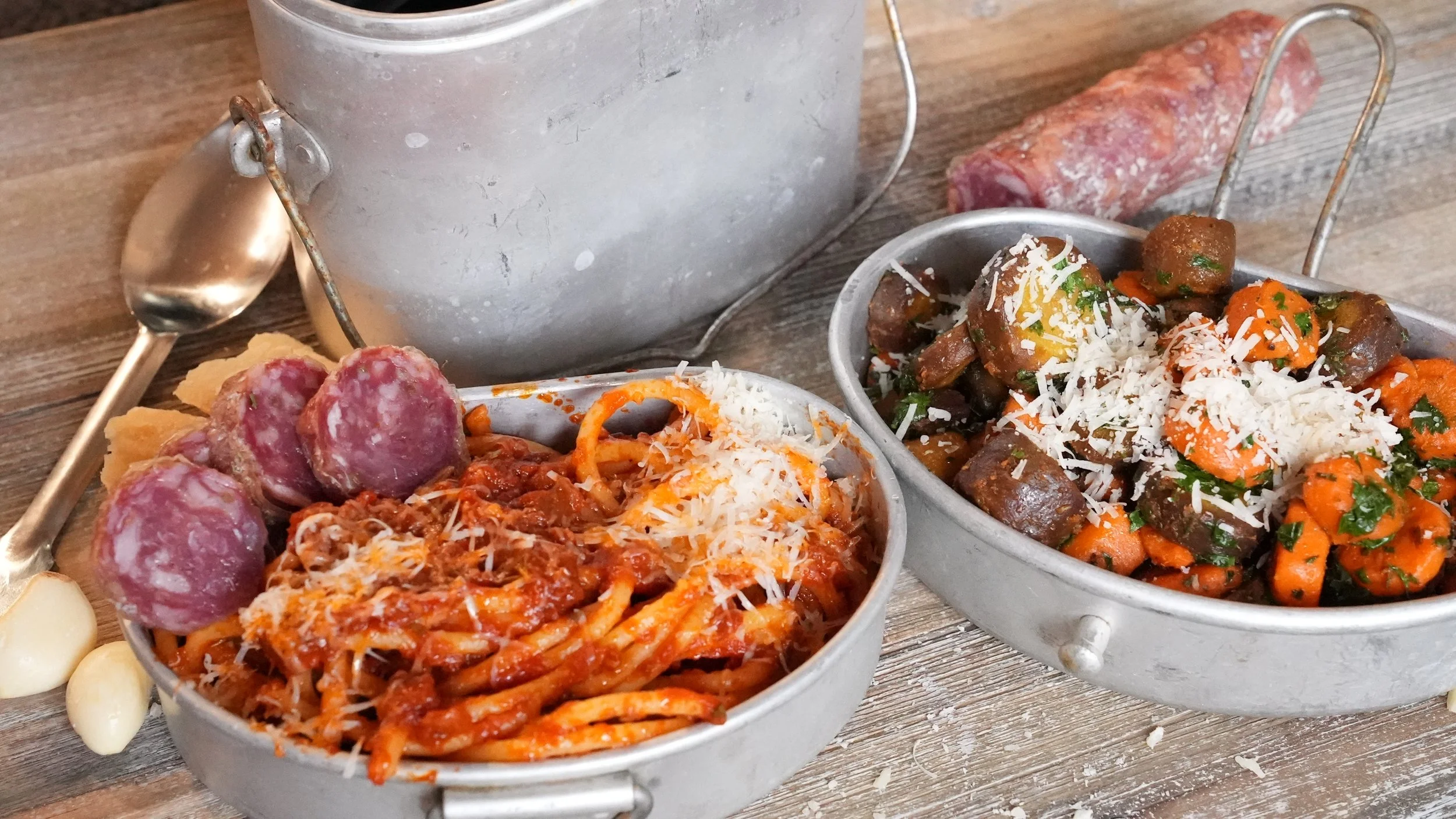 pasta with tomato sauce topped with parmesan with slices of salami in an italian wwii mess kit with sauteed purple and orange carrots topped with parmesan cheese in an italian wwii mess kit
