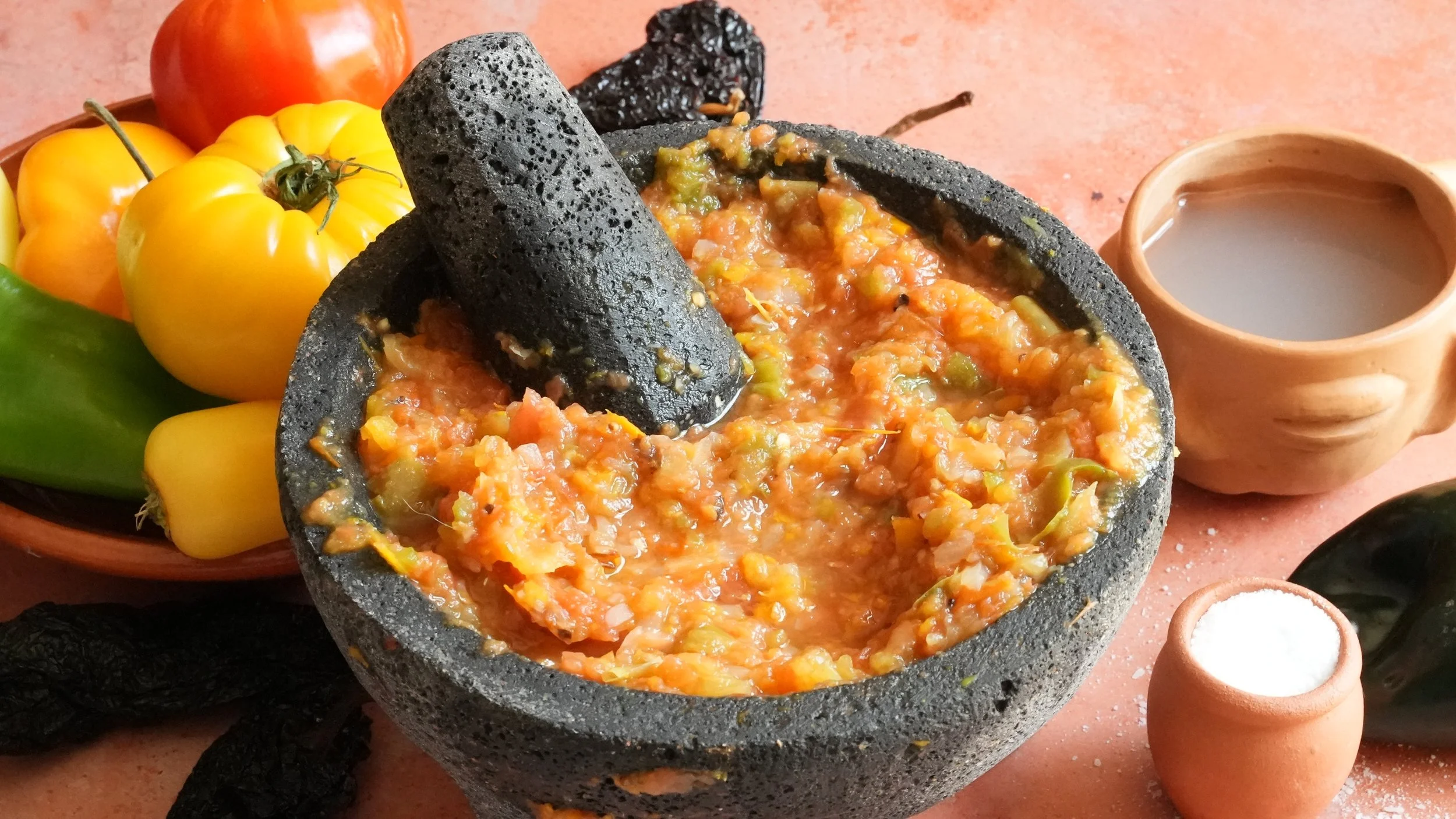 fresh salsa in a molcajete with fresh tomatoes and chiles, a cup of pulque, and a container of salt