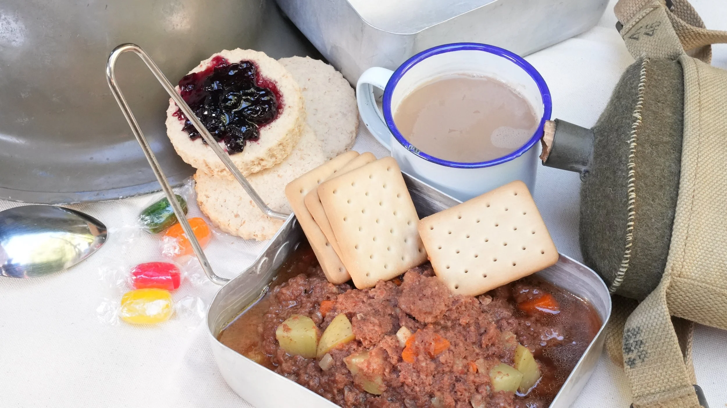 canned corned beef stew with military biscuits served with boiled sweets, round british ration scones with jam, and tea made from fannings and condensed milk