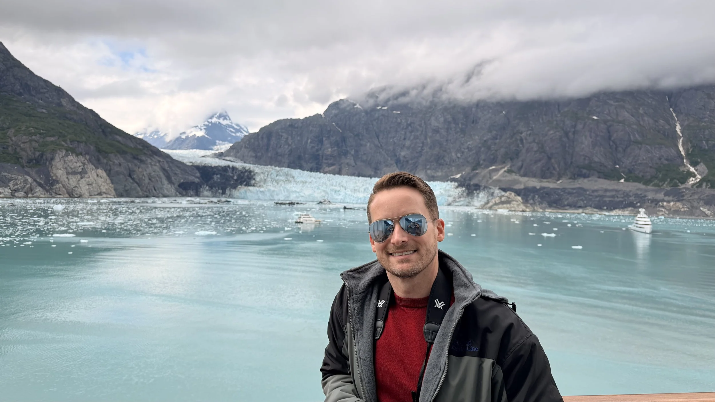 Max Miller in front of an Alaskan bay with mountains, clouds, and a glacier