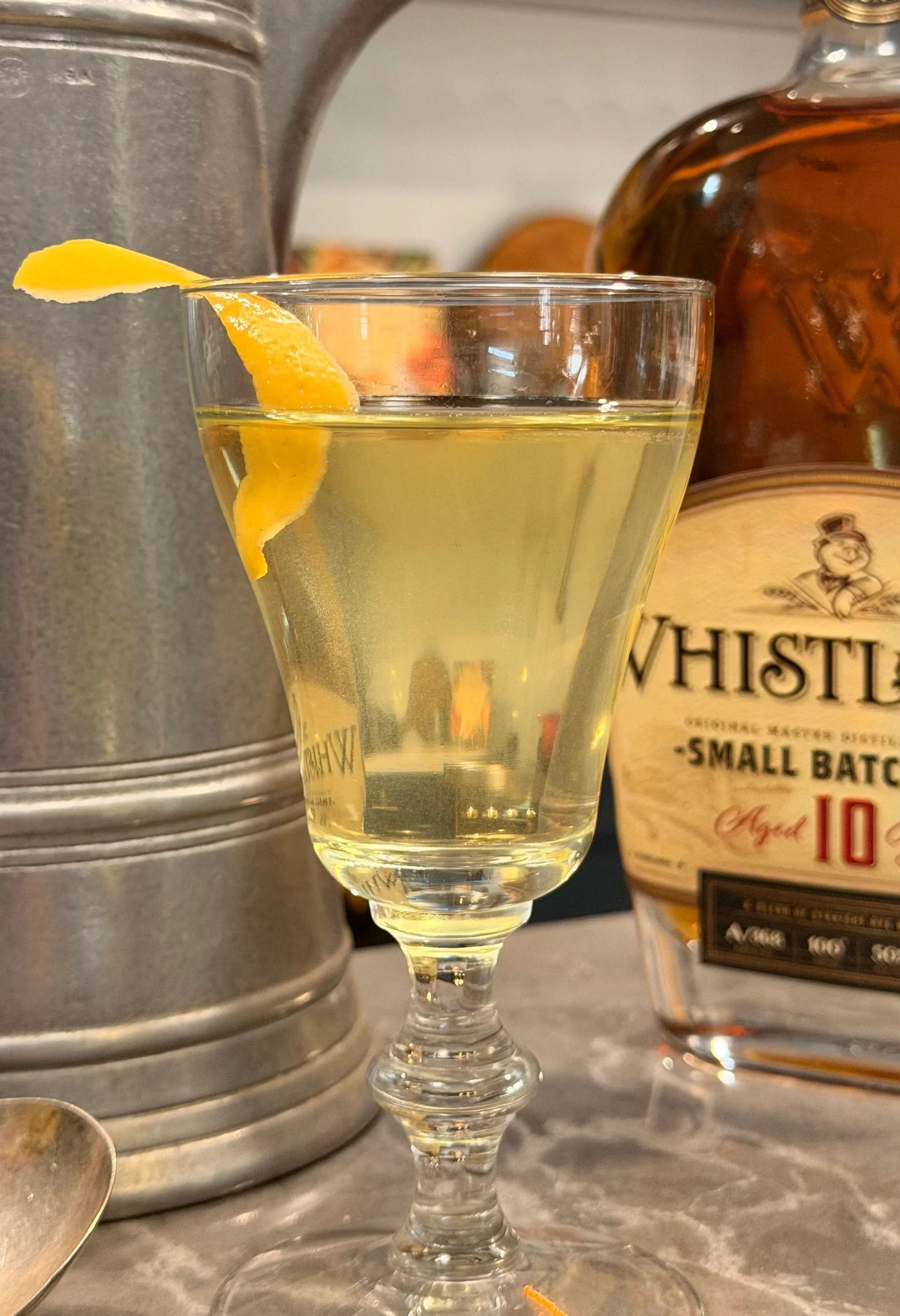 clear yellow filtered cocktail with lemon twist