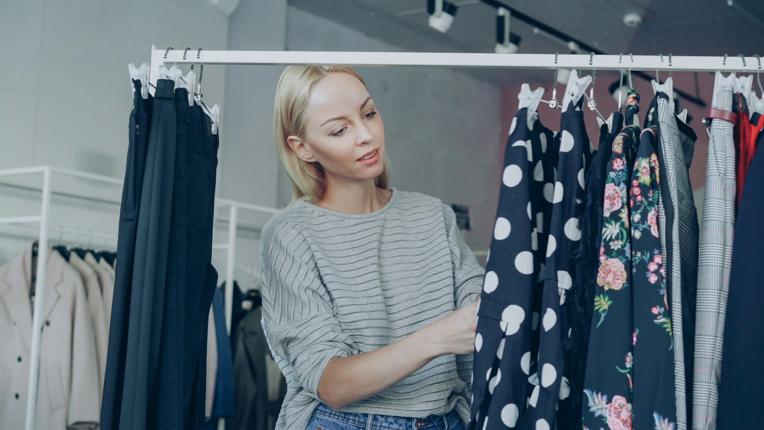 A woman looking at clothes hanging on a rail to select which one to buy or wear, to symbolise choosing masking with intentionality.