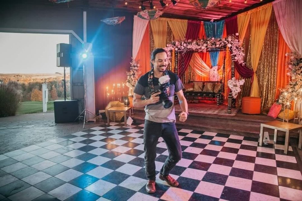 A BlackTie Brothers photographer smiling with a camera in hand inside a wedding venue
