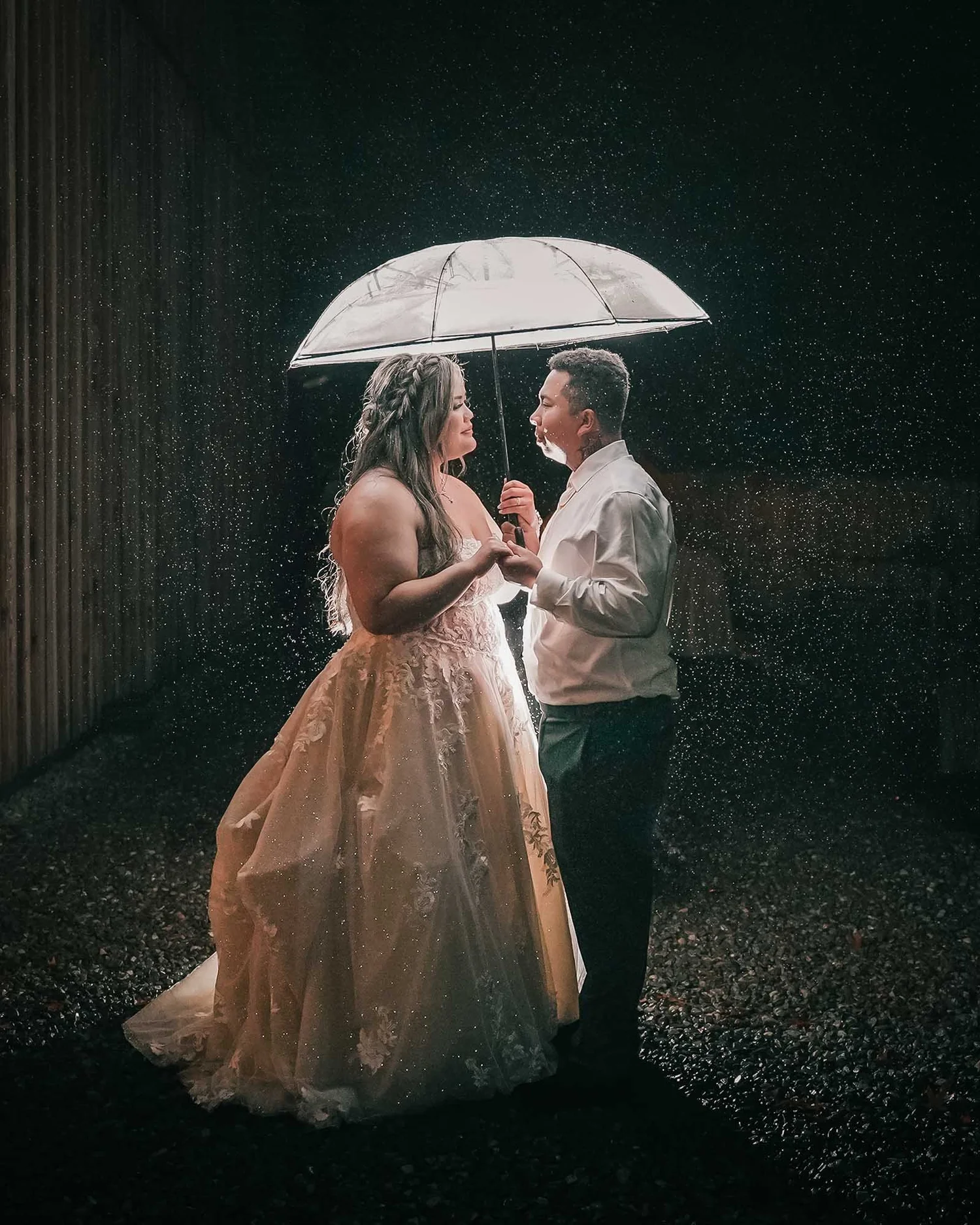 Newlyweds beneath a clear umbrella in a dramatic nighttime rain portrait by BlackTie Brothers