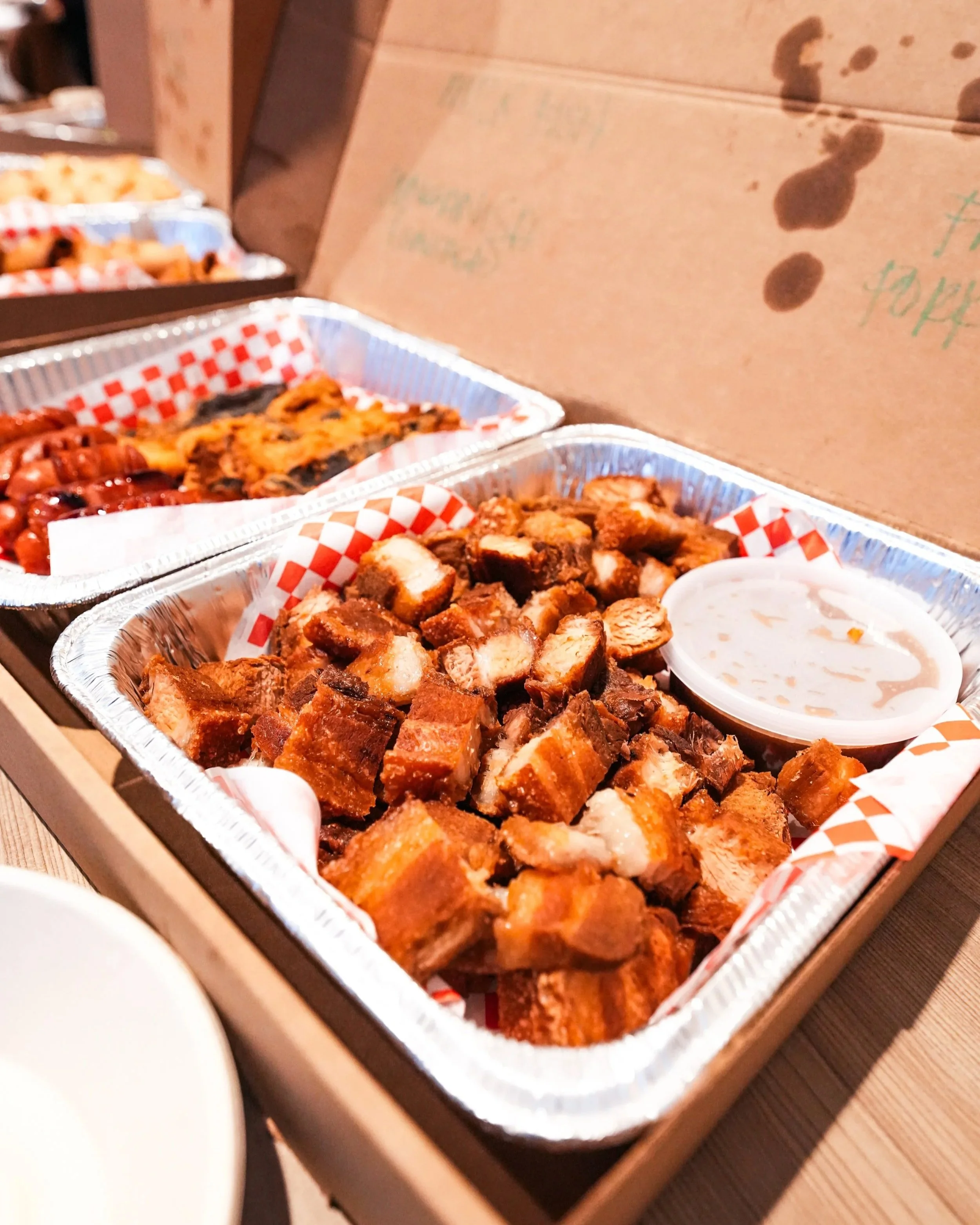 A tray of fried pork belly also known as limepo or lechon kawali with a side of spicy vinegar and other food trays such as longanisa